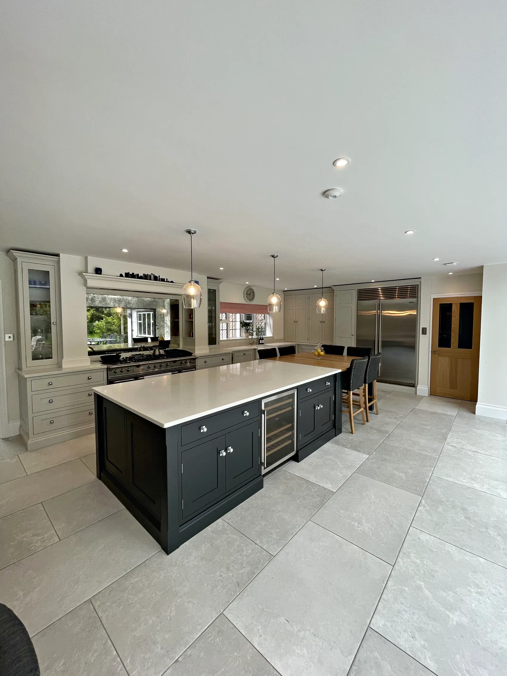 Open plan kitchen with a charcoal navy island, pale grey cabinetry, a range under a canopy and a steel fridge