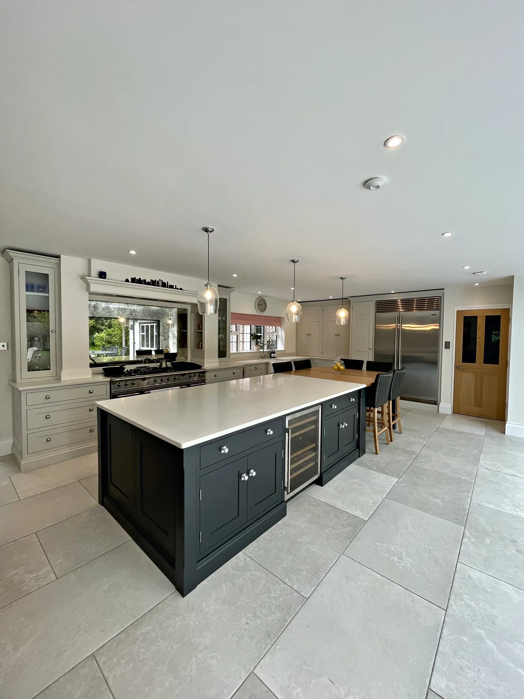 Charcoal island with a white quartz top before a range wall, a steel fridge freezer and oak doors