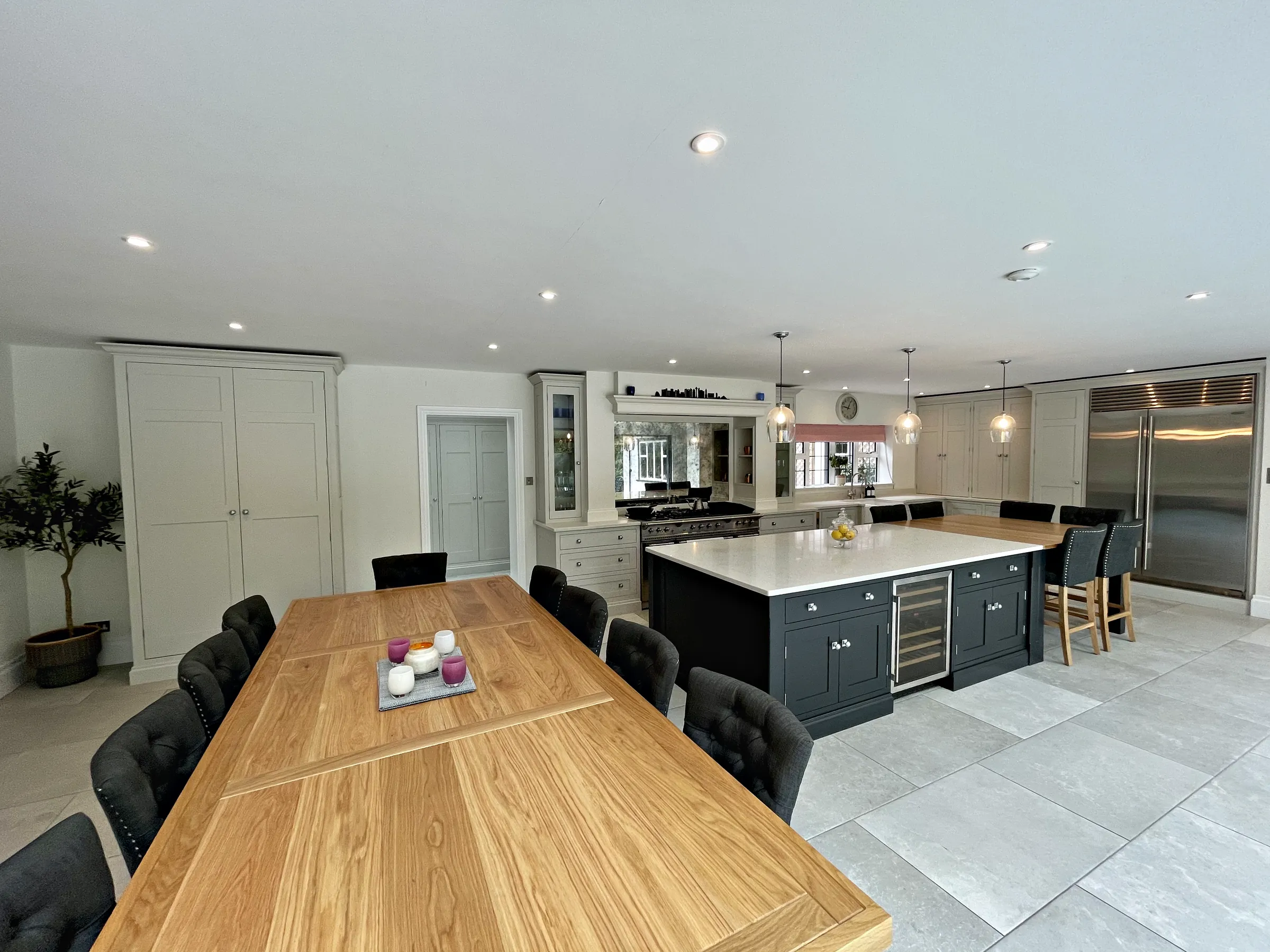 Open plan kitchen and dining room with an oak table, a charcoal island and a pale grey range wall