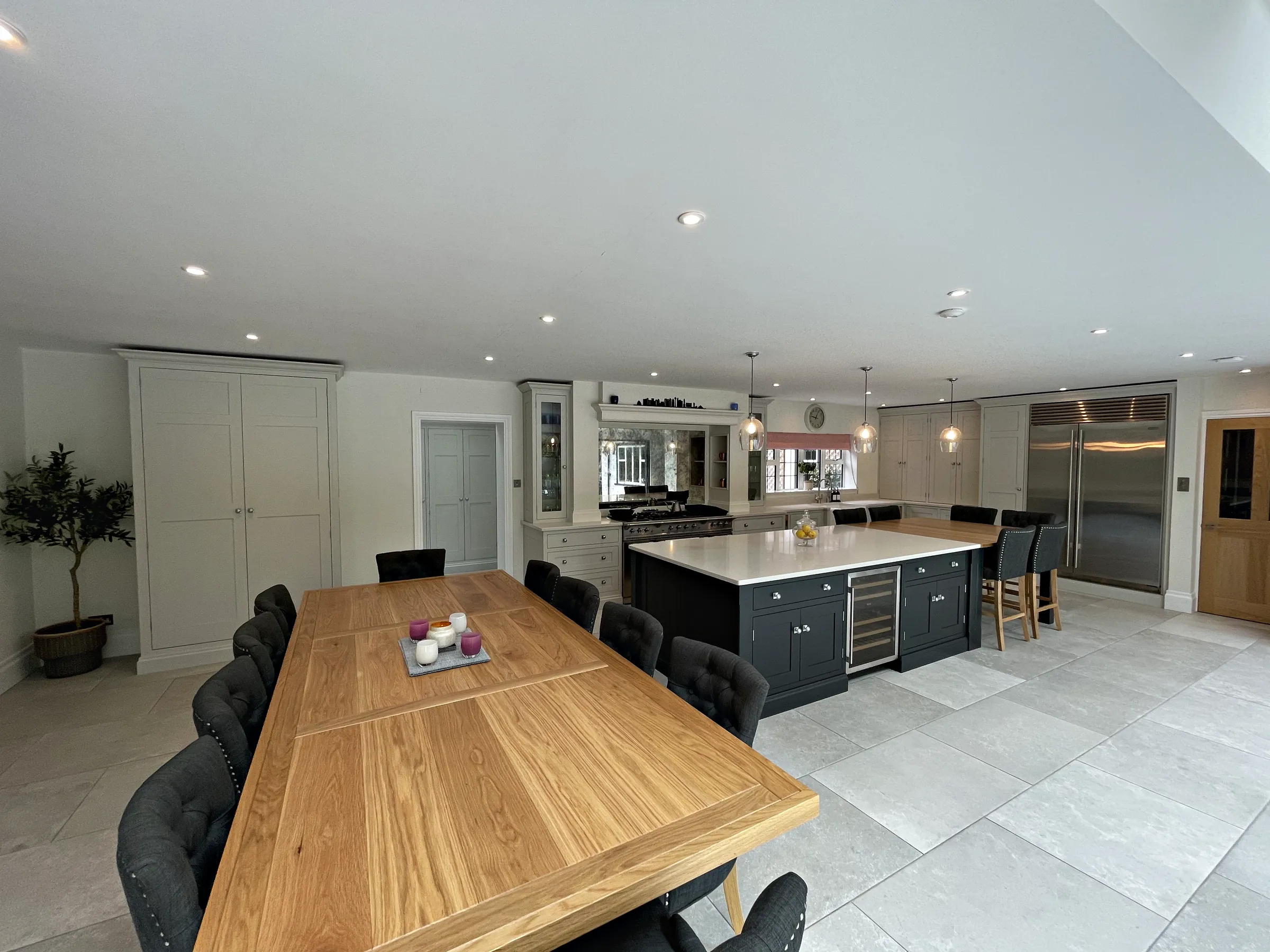 Kitchen and dining room with a pale grey larder cupboard, a charcoal island and a range wall beyond