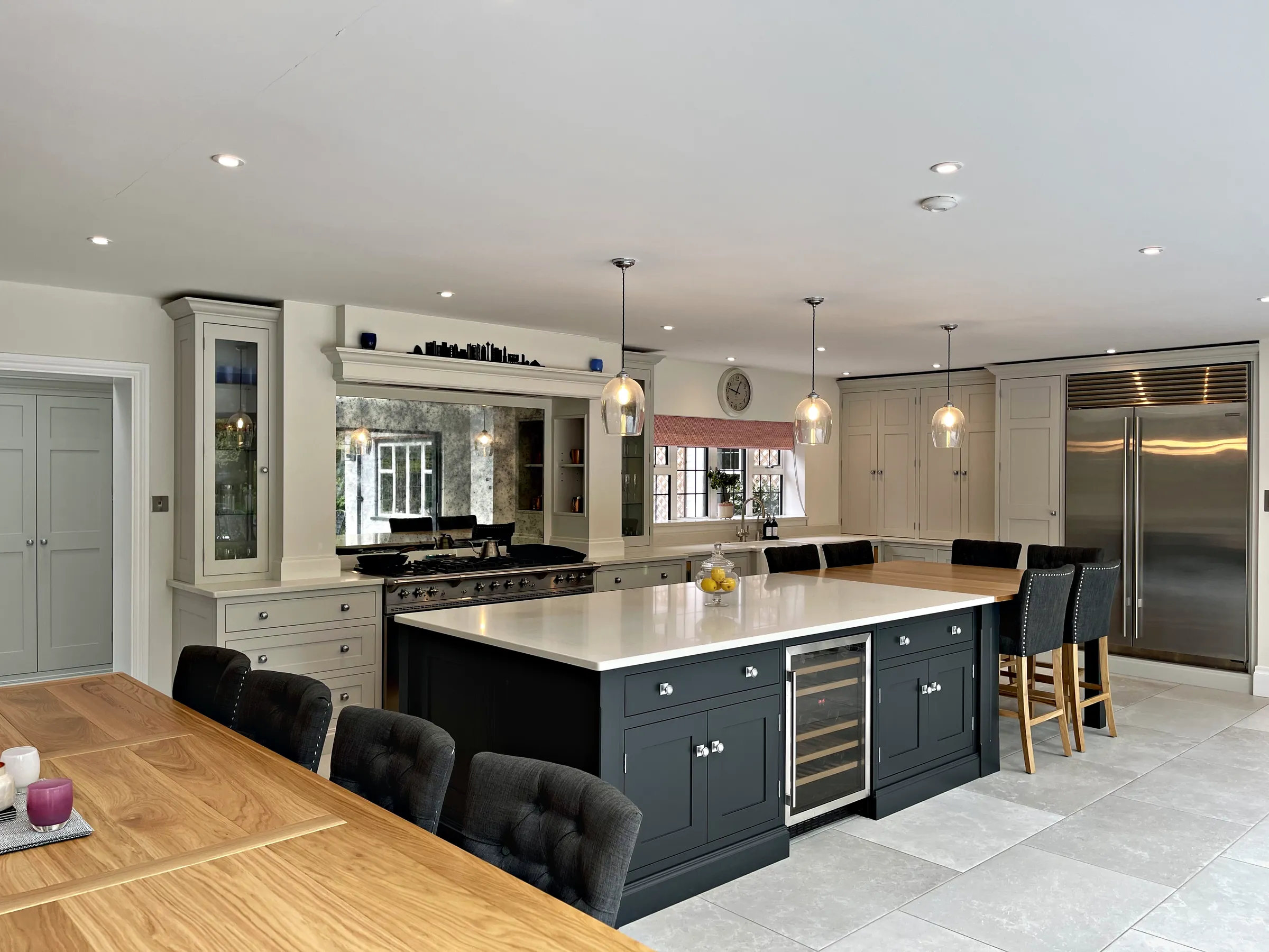 Charcoal island before a range wall with a mirrored splashback and glazed dresser, seen past an oak dining table