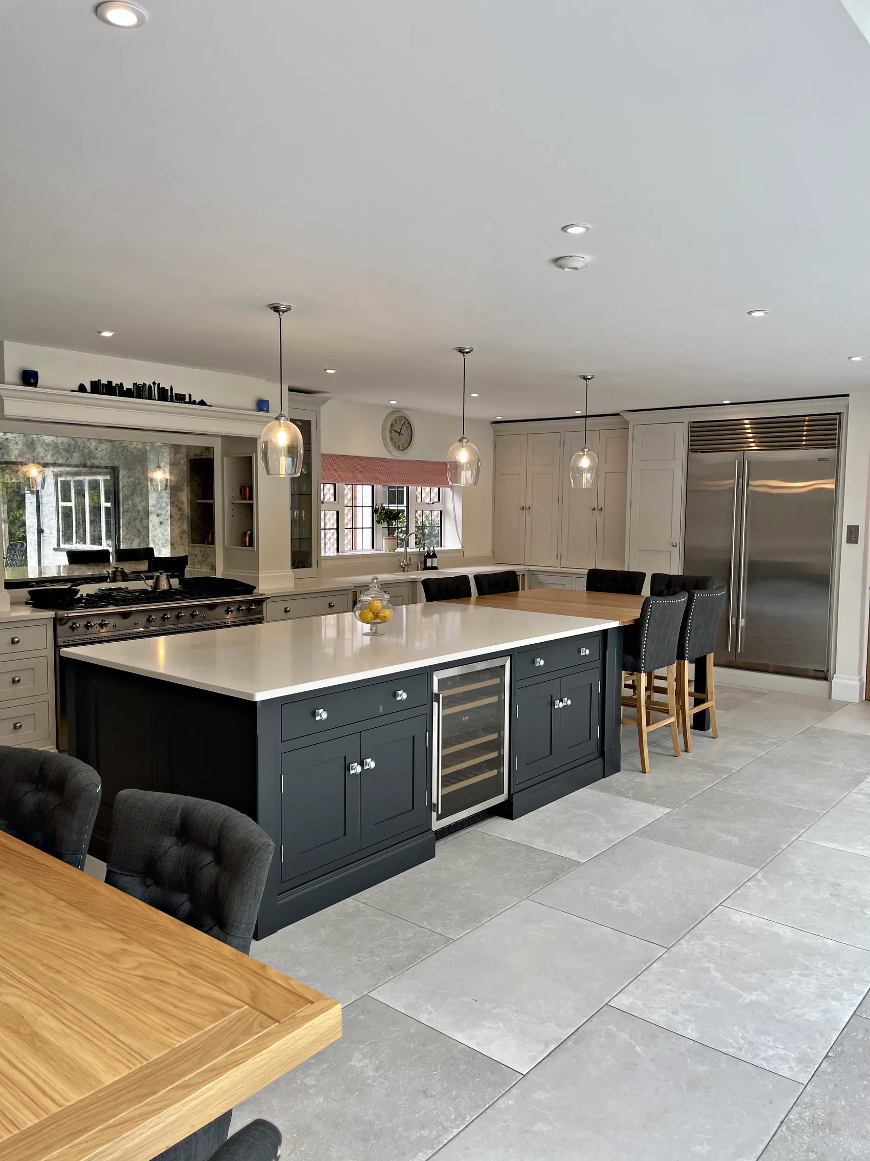 Charcoal island with a wine cooler before a range wall and steel fridge freezer, seen from the dining end
