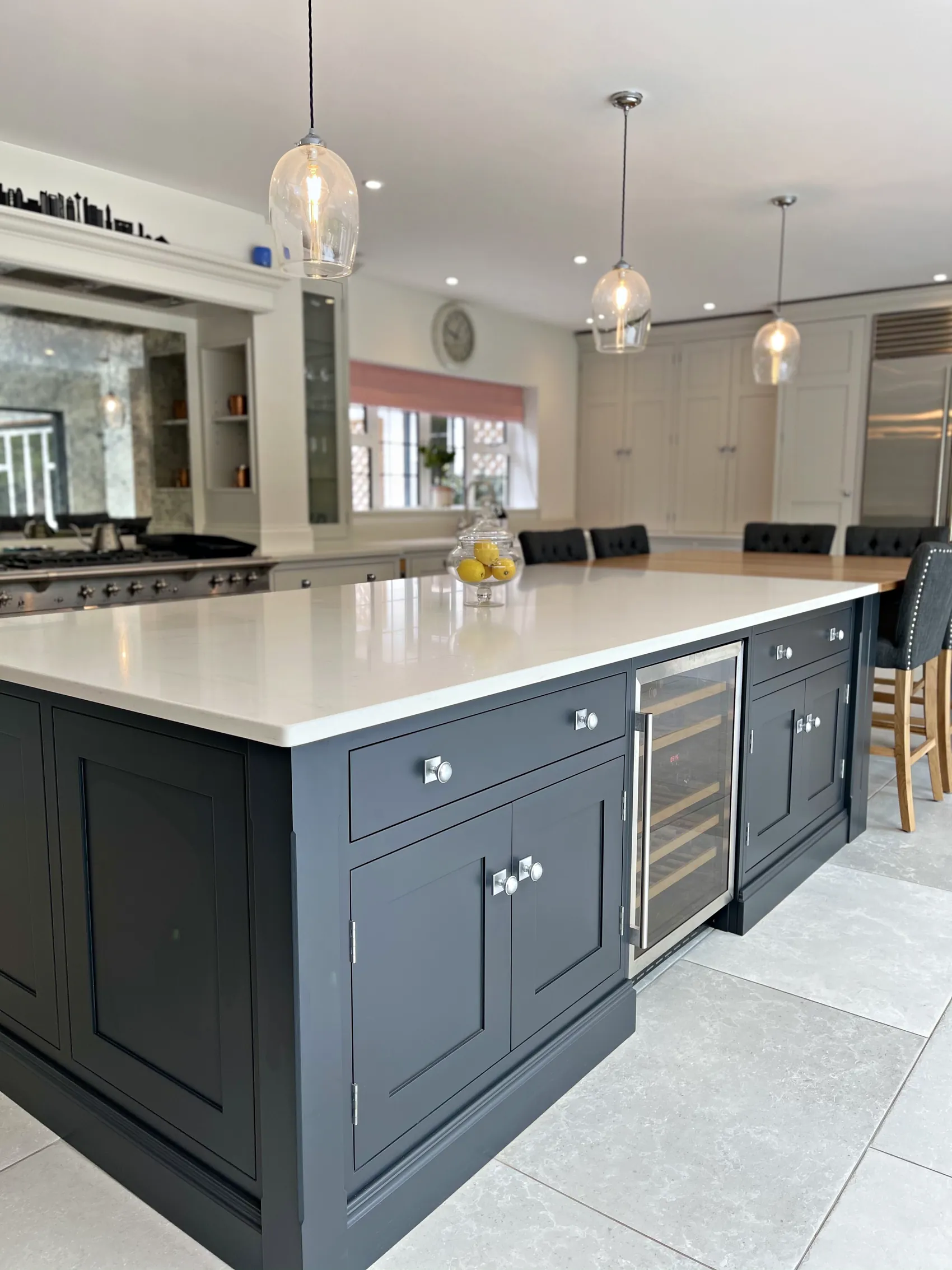 Charcoal navy island with a white quartz top and wine cooler under glass pendants