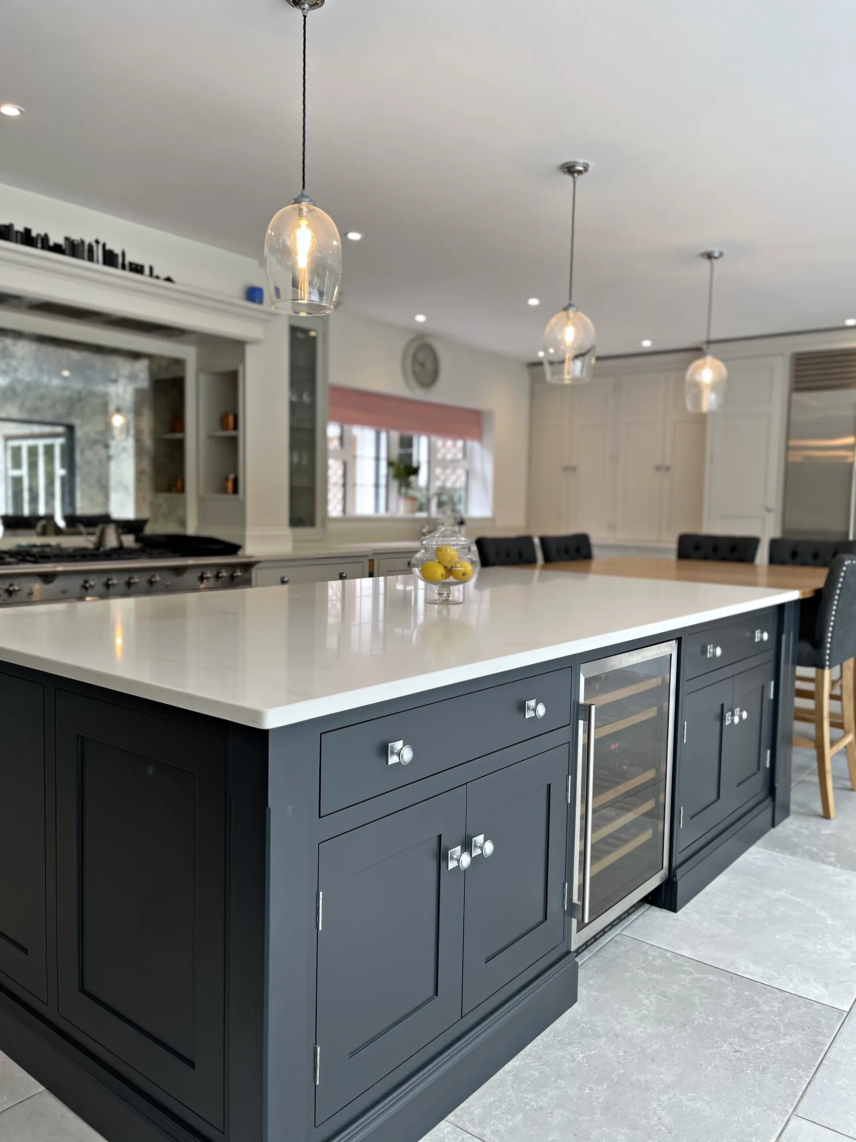 Charcoal navy island with a white quartz top and wine cooler under glass pendants, range canopy behind