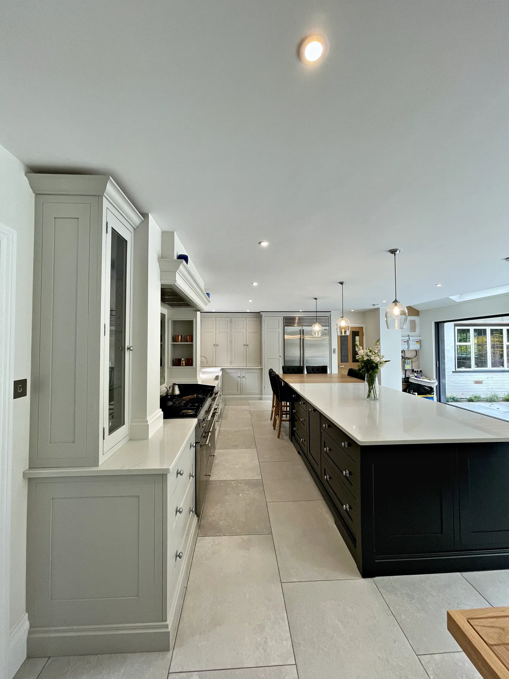 Pale grey glazed dresser and a long charcoal island looking down a bright kitchen