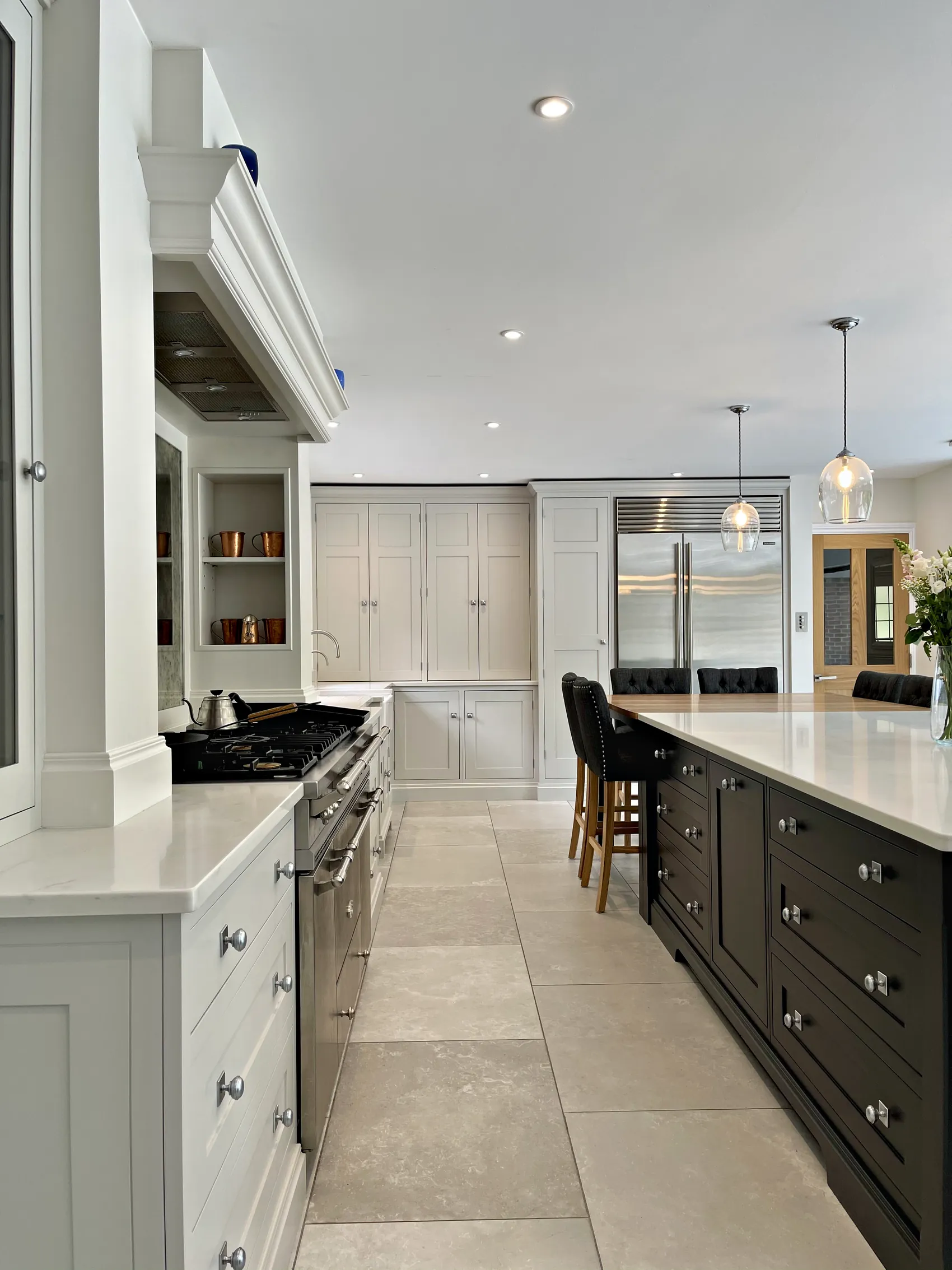 View past a range cooker to a wall of tall pale grey cupboards, a steel fridge and a charcoal island