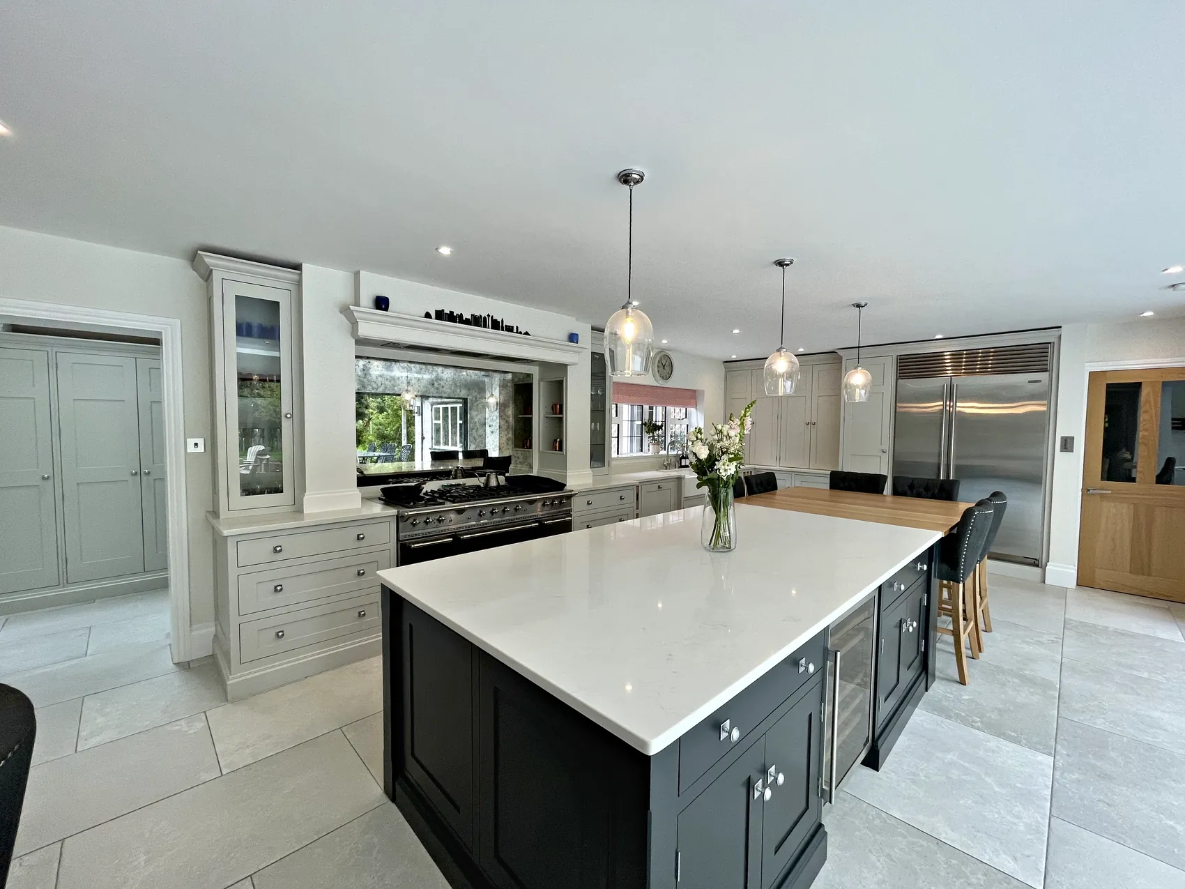 Charcoal island with a white quartz top before a range wall with a mirrored splashback, glazed dresser and steel fridge