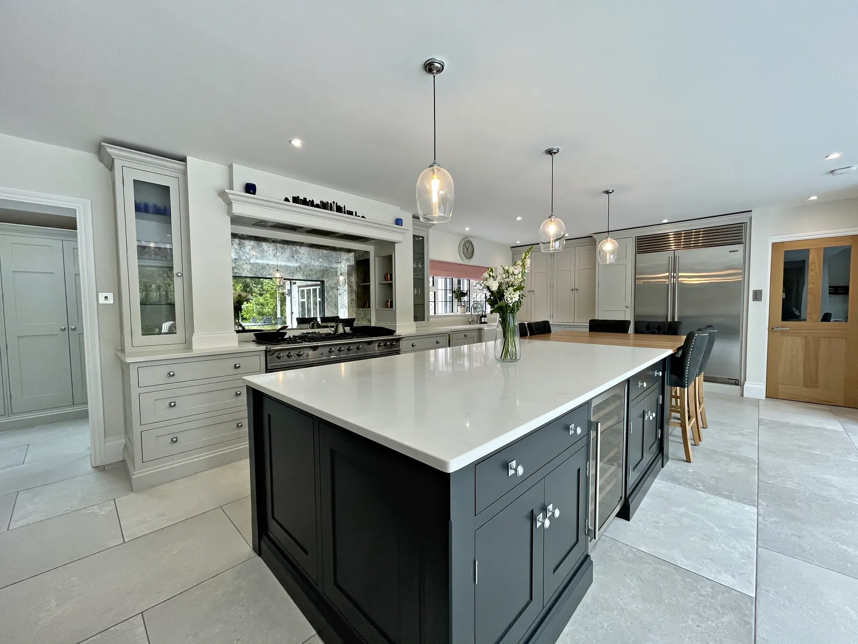 Charcoal island before a range wall with an antiqued mirror splashback, a glazed dresser and tall cupboards