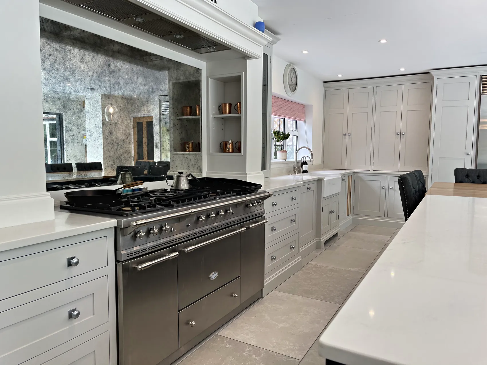 Range cooker under a painted mantel with an antiqued mirror splashback, copper pans on lit shelves and a sink beyond