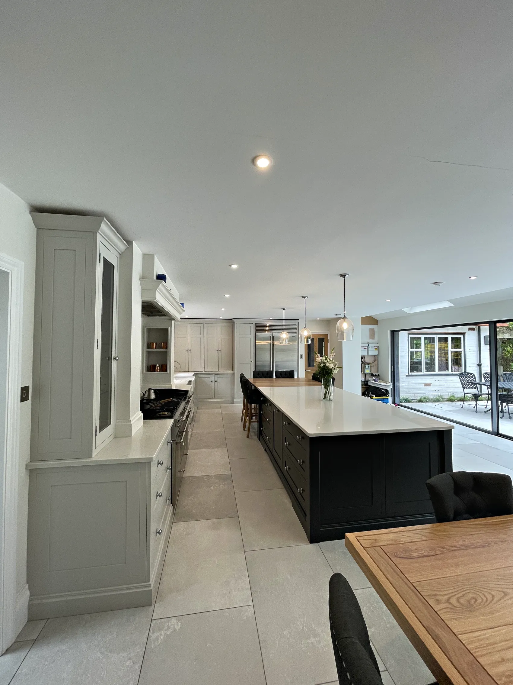 Long pale grey kitchen with a glazed dresser and range run beside a charcoal island leading to garden doors