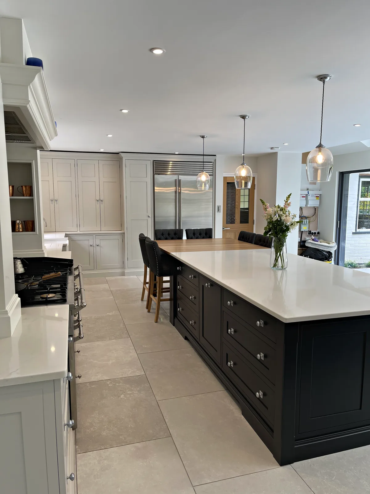 Charcoal island with bar stools before a wall of tall pale grey cupboards and a steel fridge