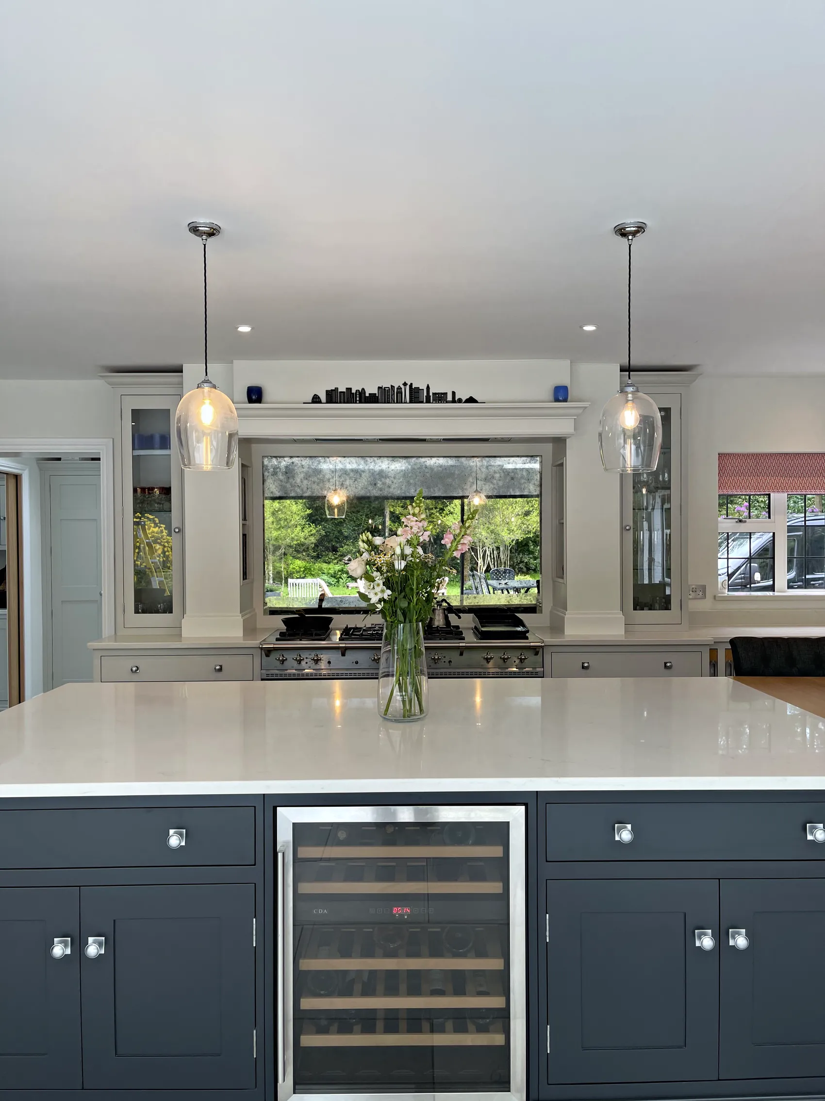 Charcoal navy island front with a wine cooler and white quartz top under glass pendants, range wall beyond