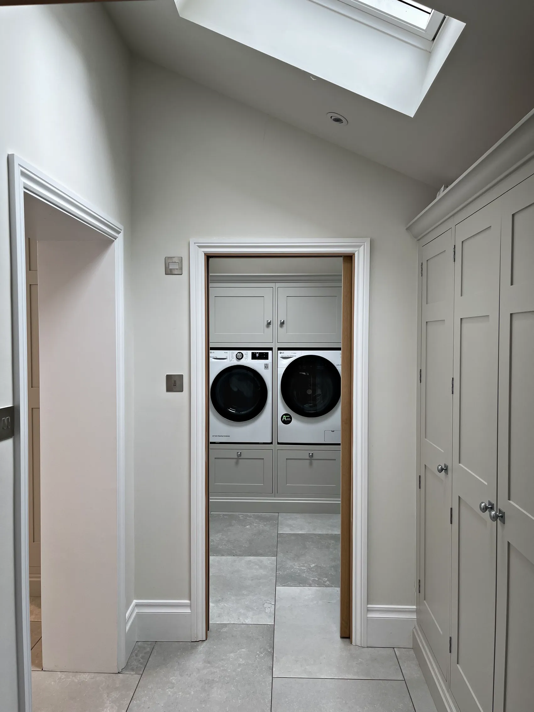 Corridor of floor to ceiling pale grey cupboards with nickel knobs leading to a utility room