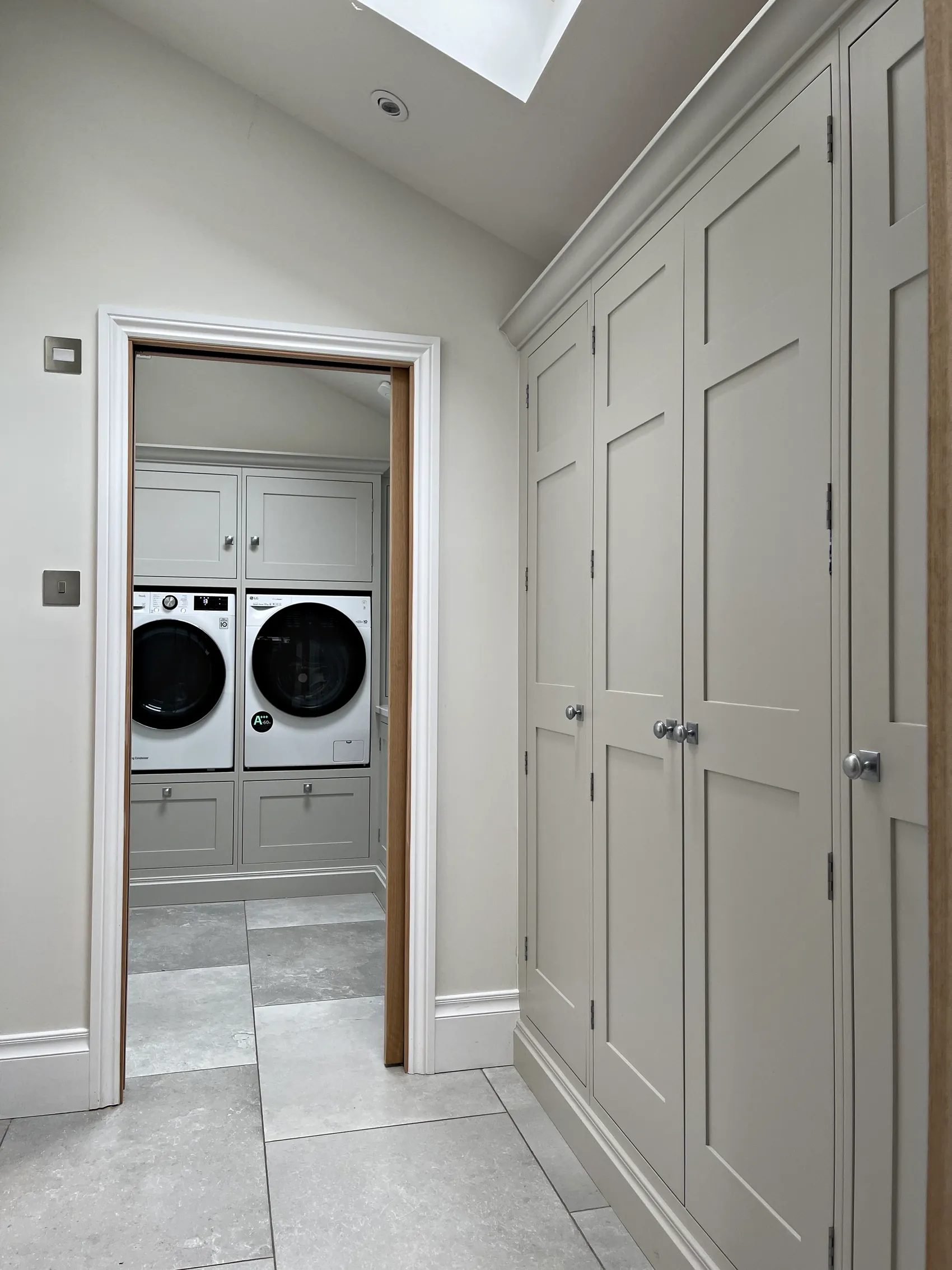 Corridor lined with floor to ceiling pale grey cupboards with nickel knobs under a roof window