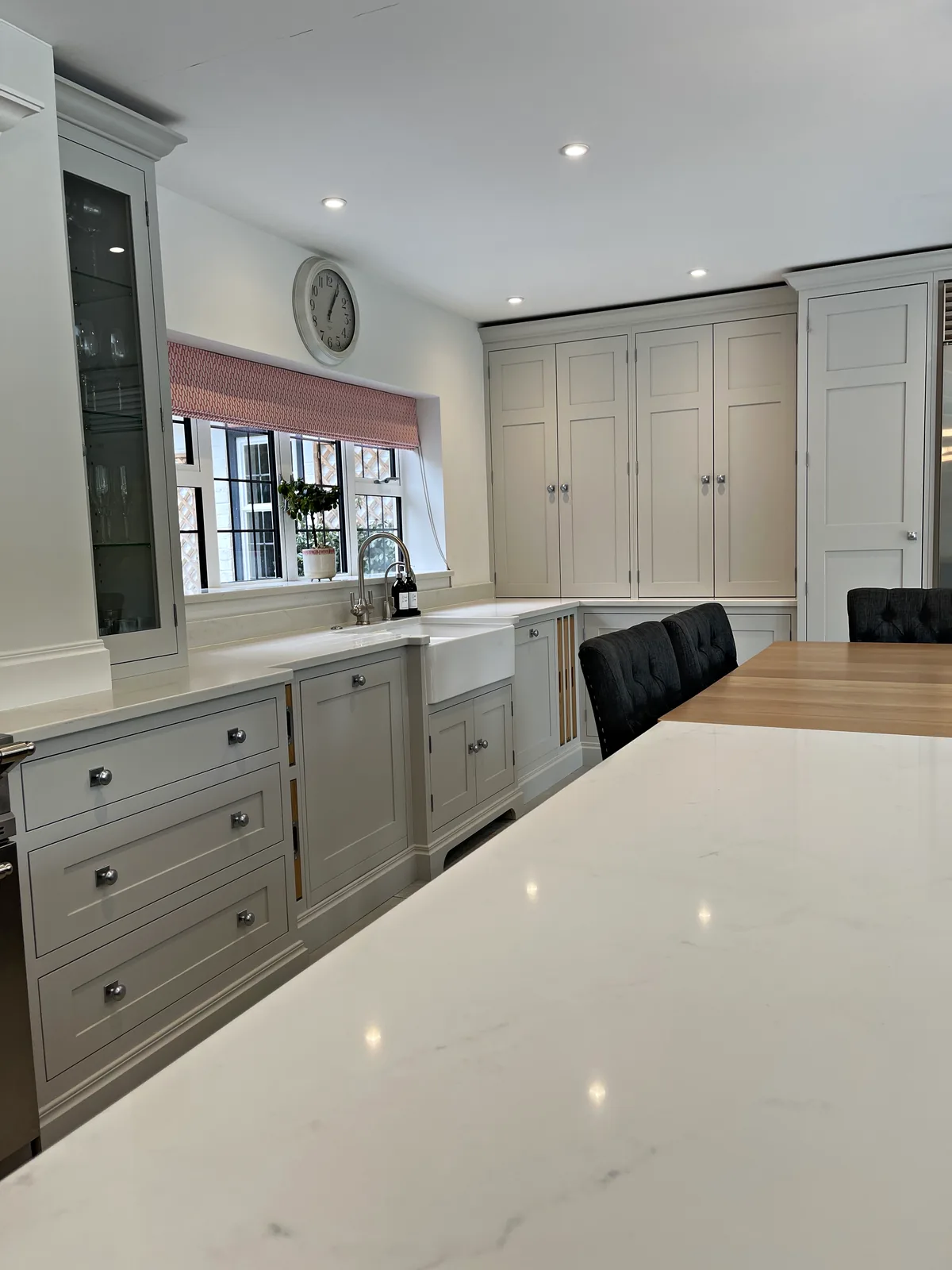 White quartz island top with a pale grey sink run and tall painted cupboards beyond