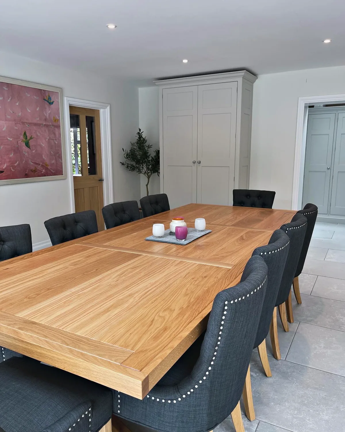 Long oak dining table made for Munstead Plat, with upholstered chairs on a pale stone floor