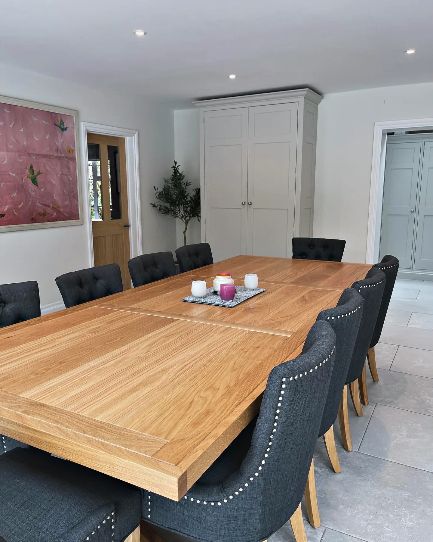 Long oak dining table made for Munstead Plat, with upholstered chairs on a pale stone floor