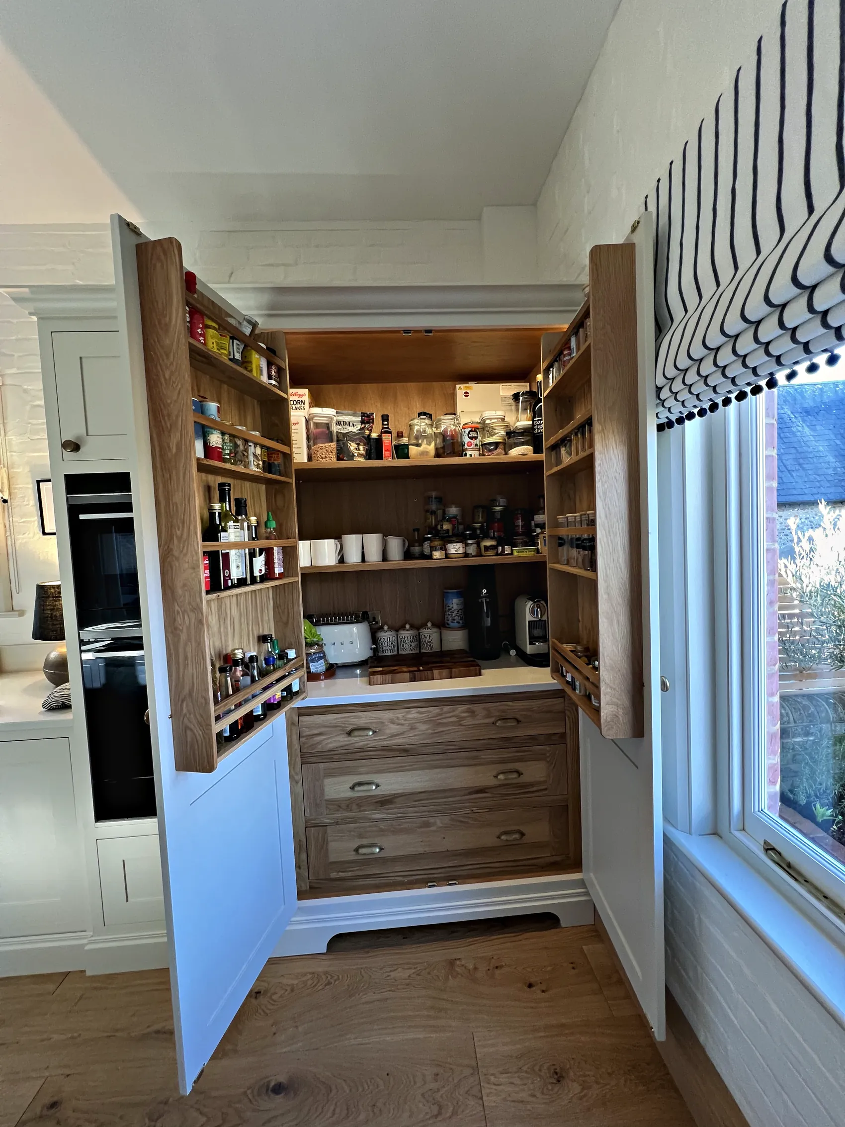 Larder cupboard open on oak lined shelves and door spice racks above oak drawers