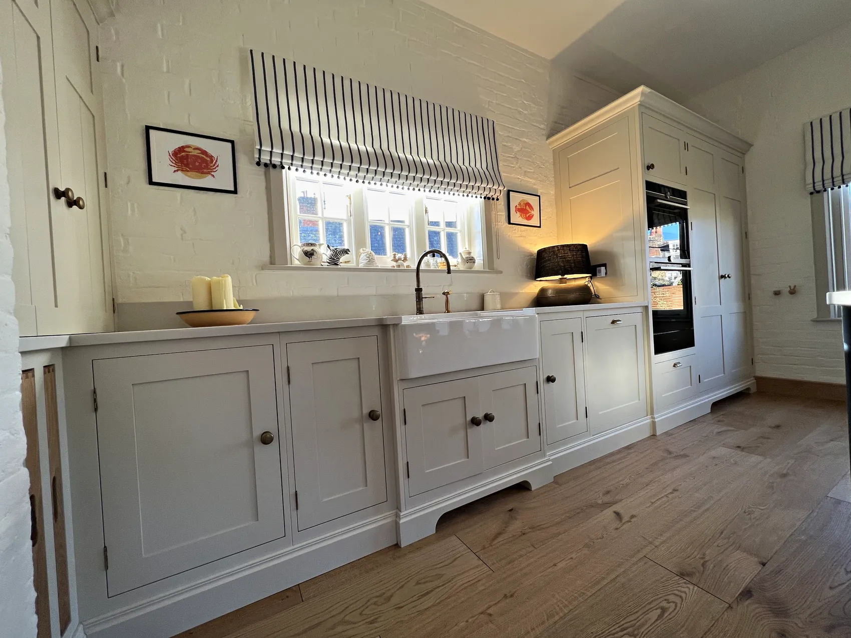 Cream Belfast sink run with a shaped plinth and tall oven housing against painted brick