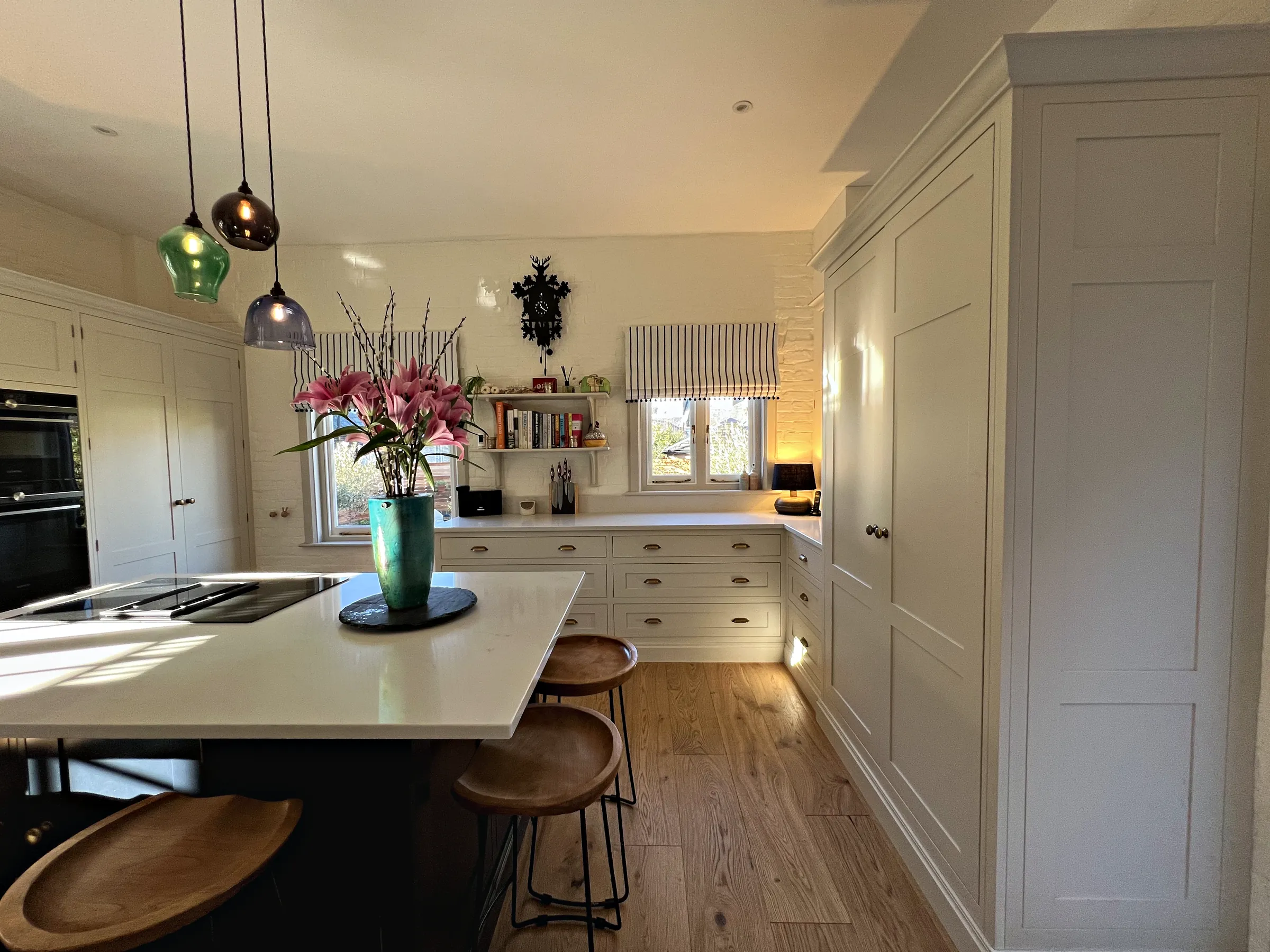 Navy island with stools in front of a tall cream larder cupboard and a run of cream drawers