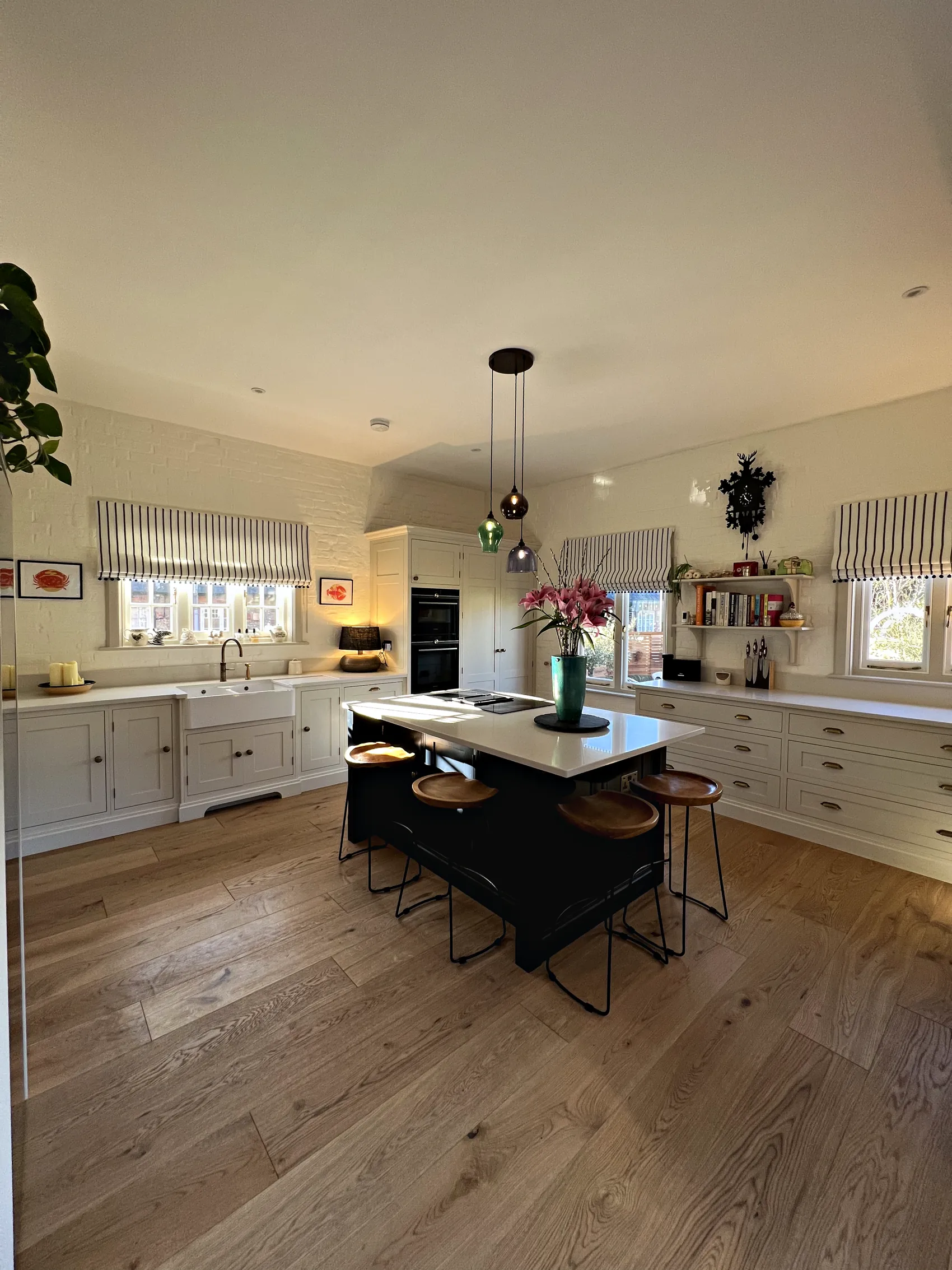 Cream kitchen with a navy island and stools, a Belfast sink run and built in ovens on oak