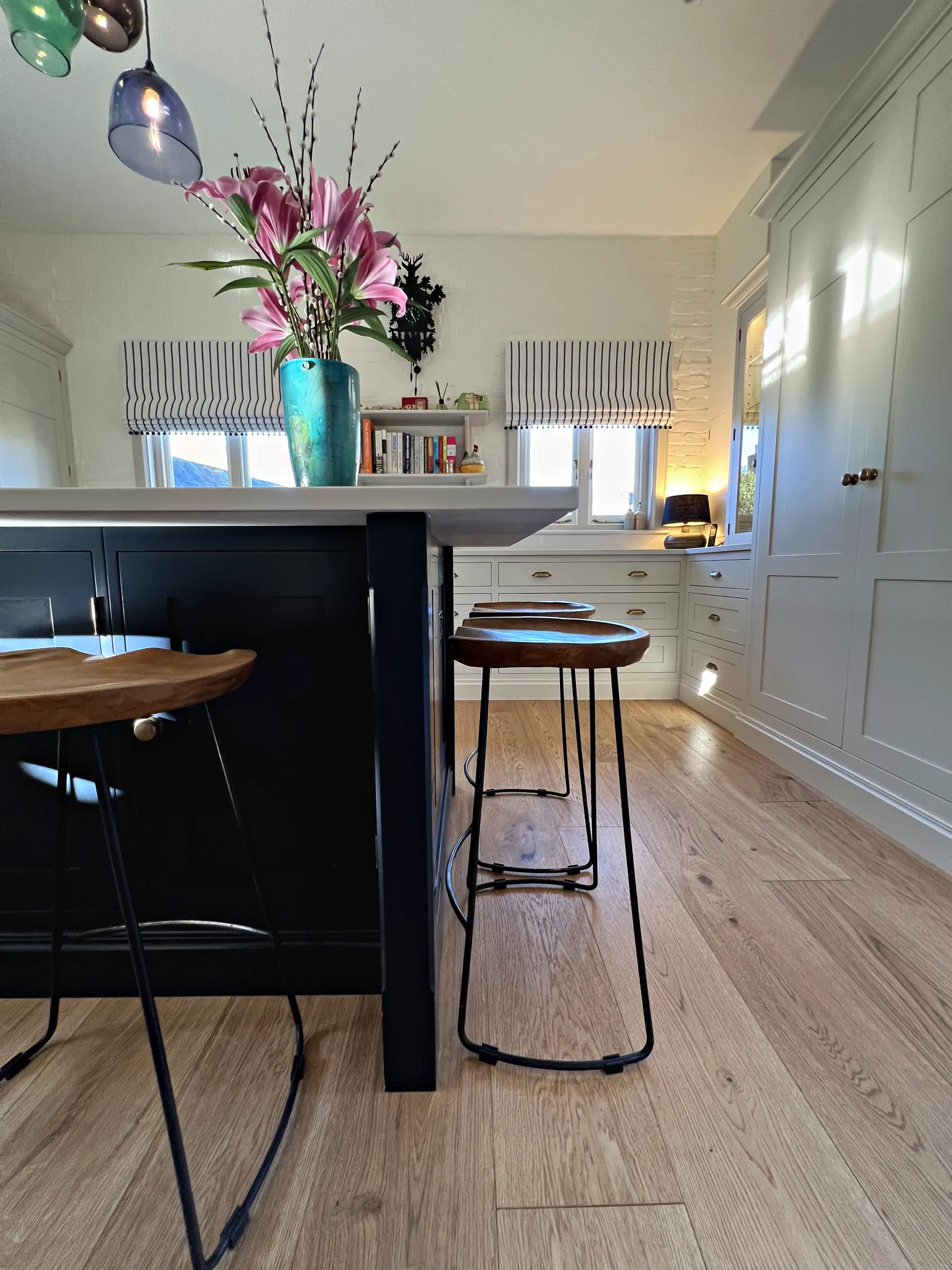 Navy island with wooden saddle stools beside tall cream cupboards on a wide oak floor