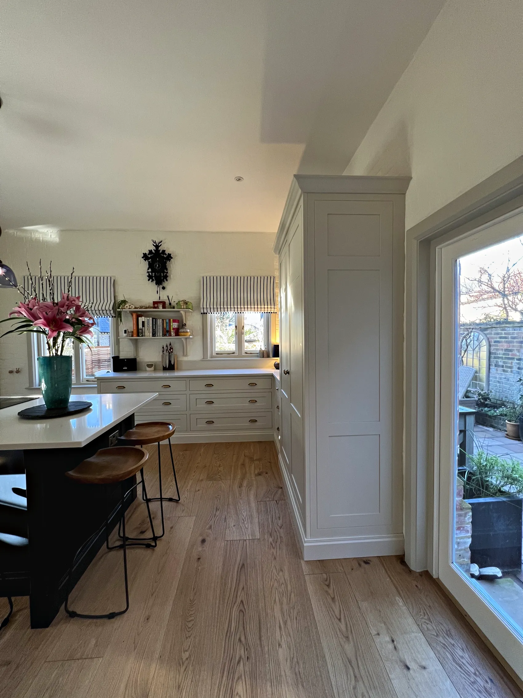 Tall cream cupboard beside the garden doors with a navy island and cream drawer run beyond