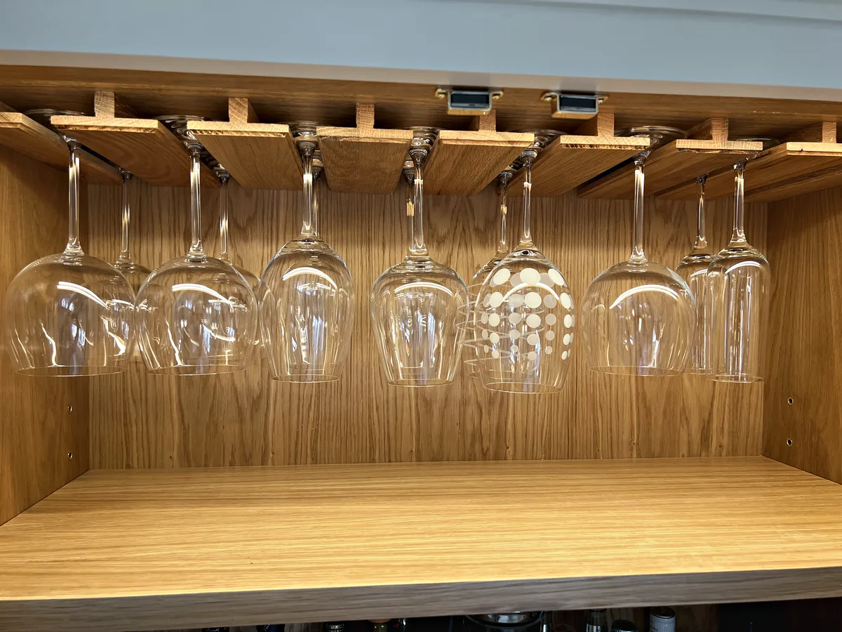 Oak lined drinks cupboard with wine glasses hanging from an oak rack
