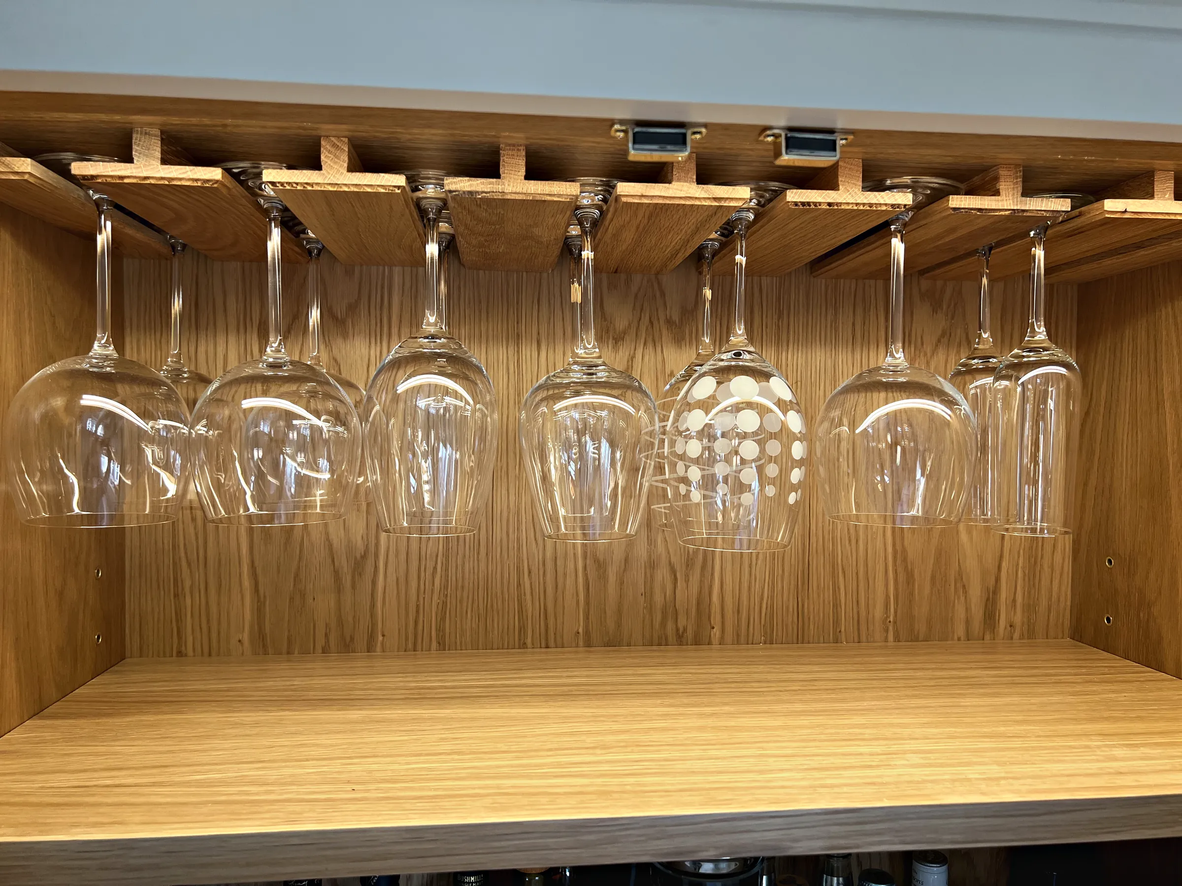 Oak lined drinks cupboard with wine glasses hanging from an oak rack