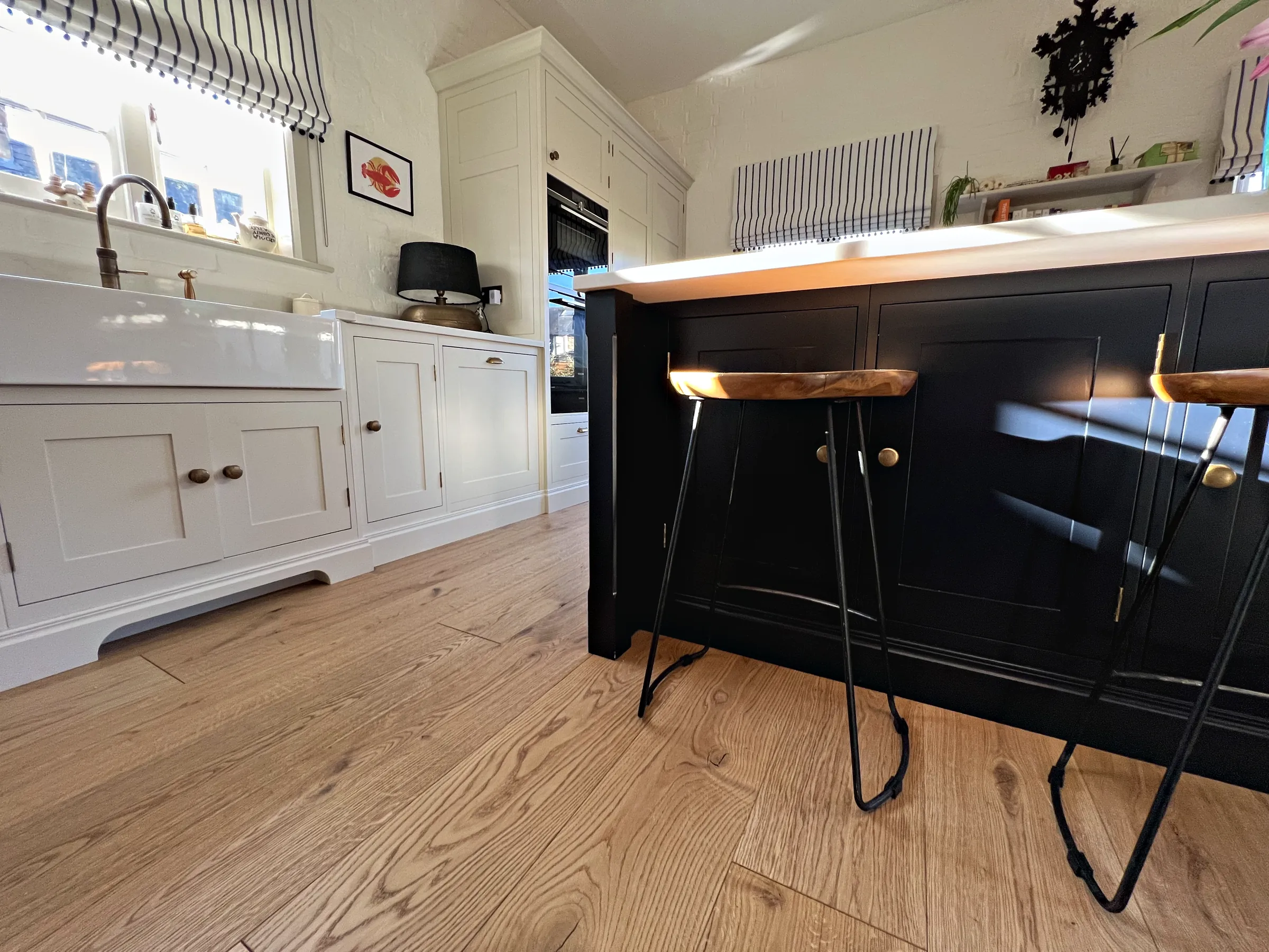 Navy island with wooden saddle stools beside a cream sink run under striped blinds on an oak floor