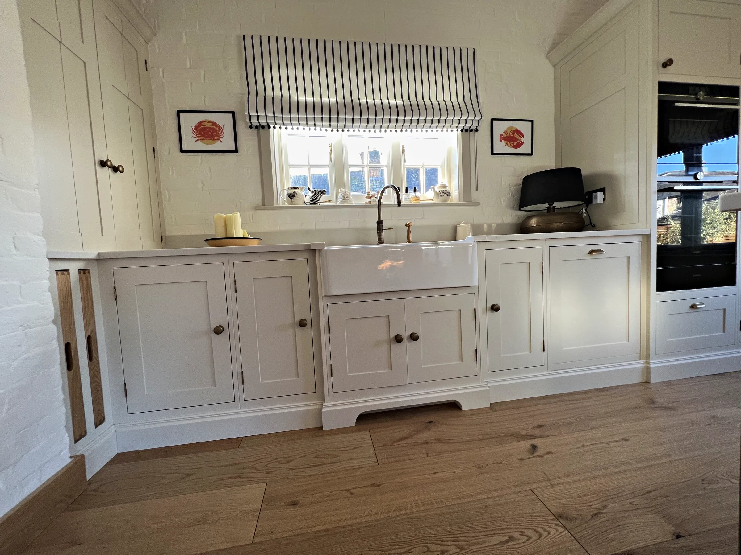 Cream Belfast sink run with a bronze tap, oak bottle slots, panelled cupboards and a shaped plinth
