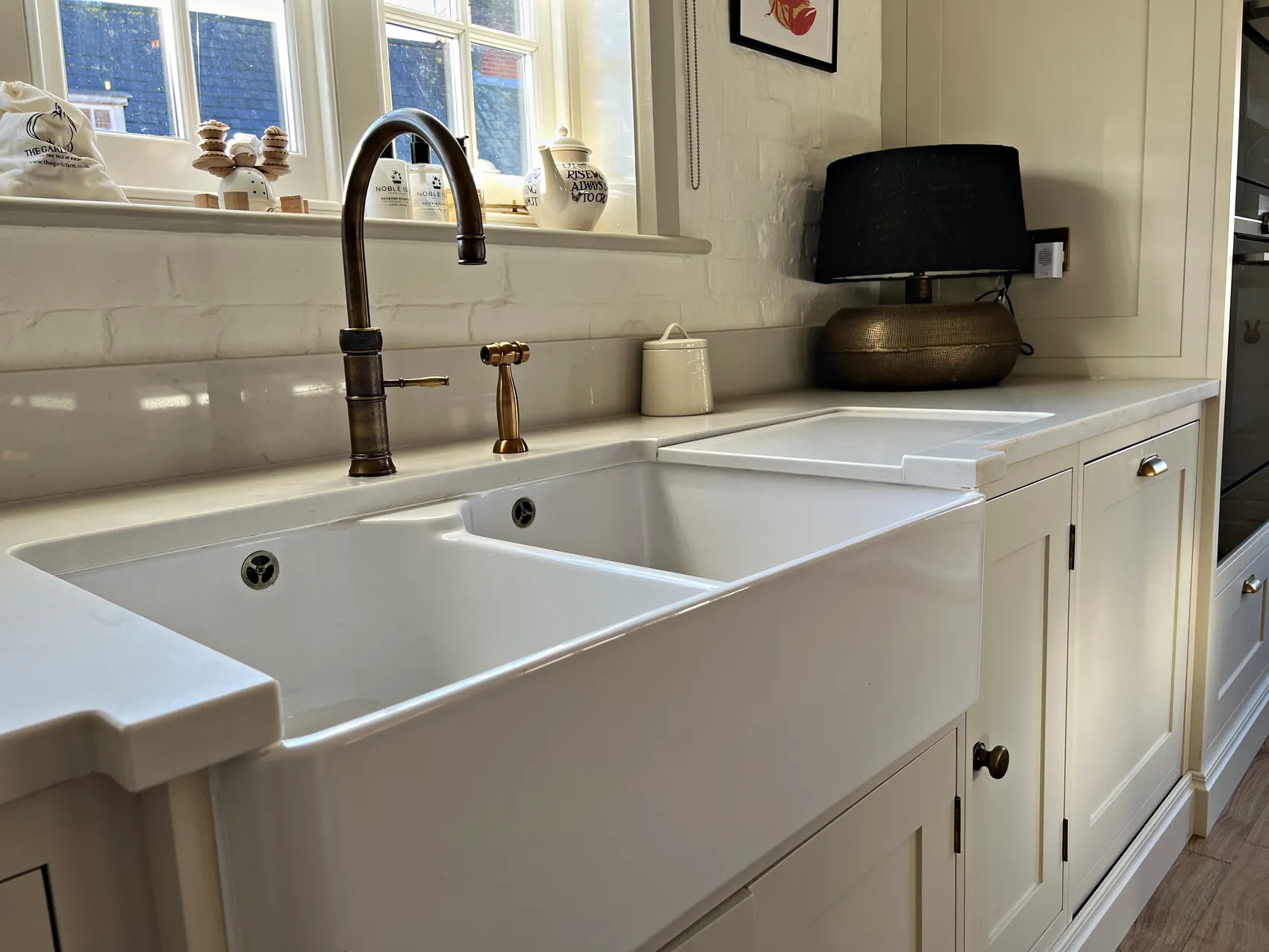 Bronze tap over a double ceramic Belfast sink set into cream cabinetry under a window
