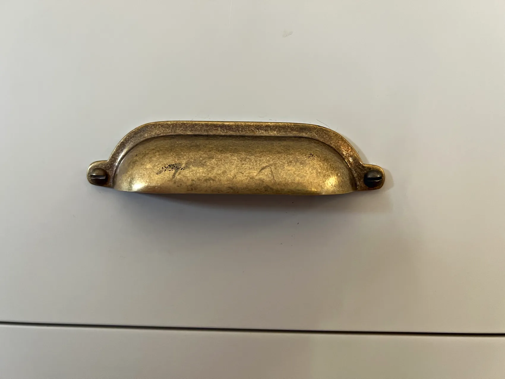Antique brass cup handle on a cream painted in frame drawer