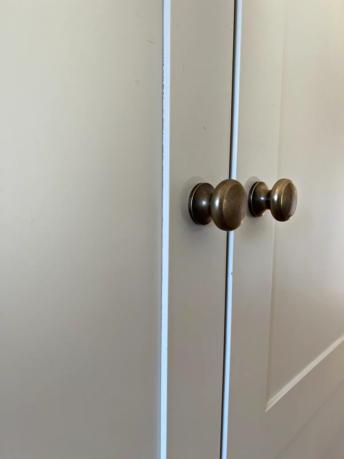 Pair of antique bronze knobs on a tall cream painted cupboard