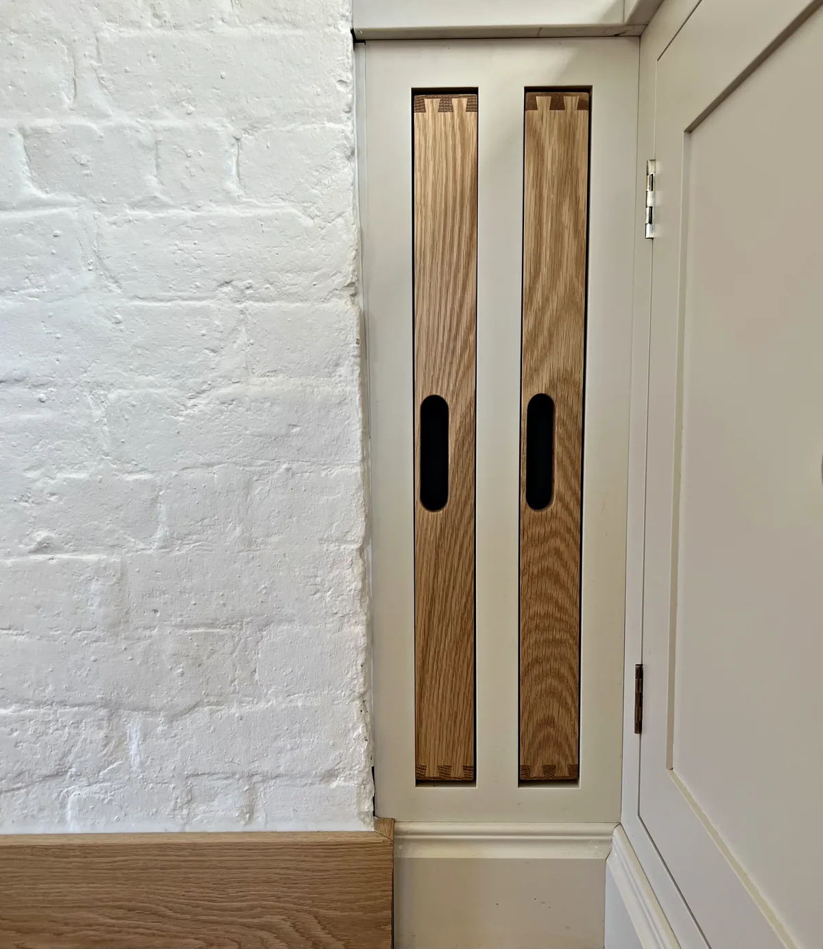 Oak tray slots set into cream cabinetry beside a painted brick wall