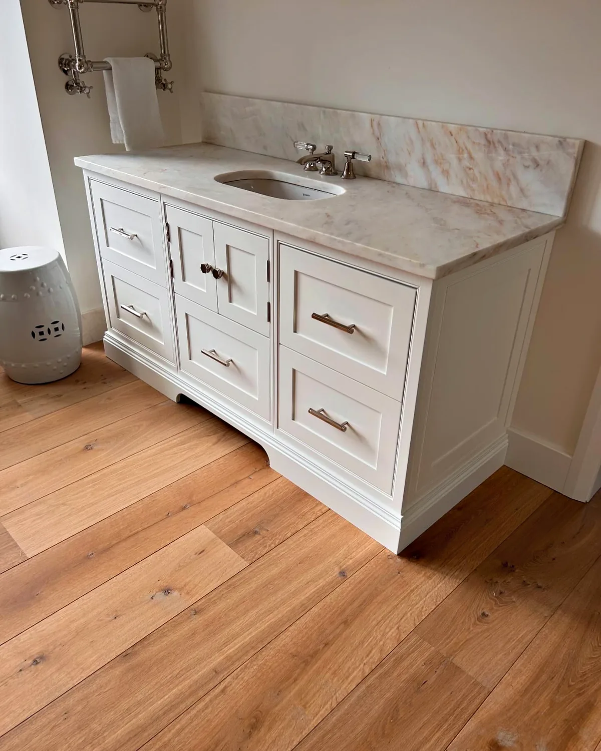 White painted vanity unit with drawers and cupboards, a pink veined marble top and nickel bar handles