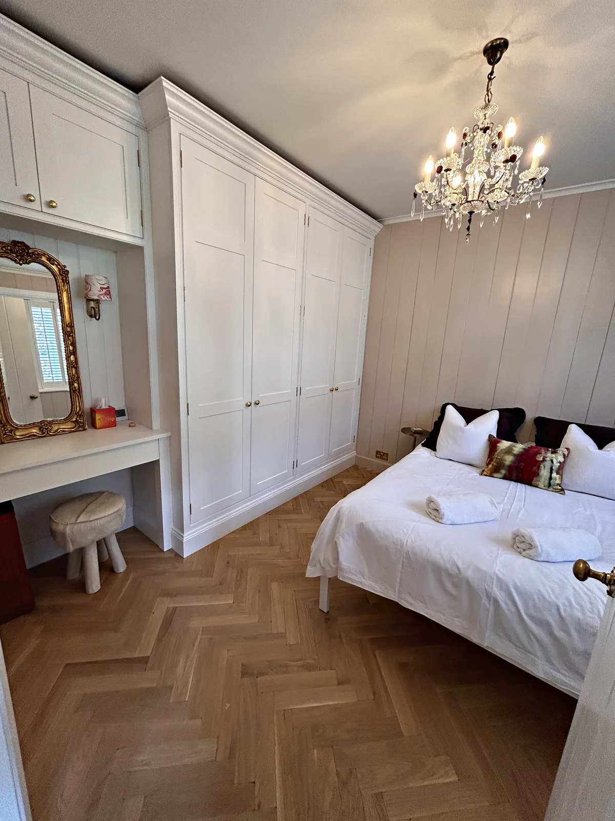 White fitted wardrobes with a dressing table alcove in a panelled bedroom with a herringbone floor