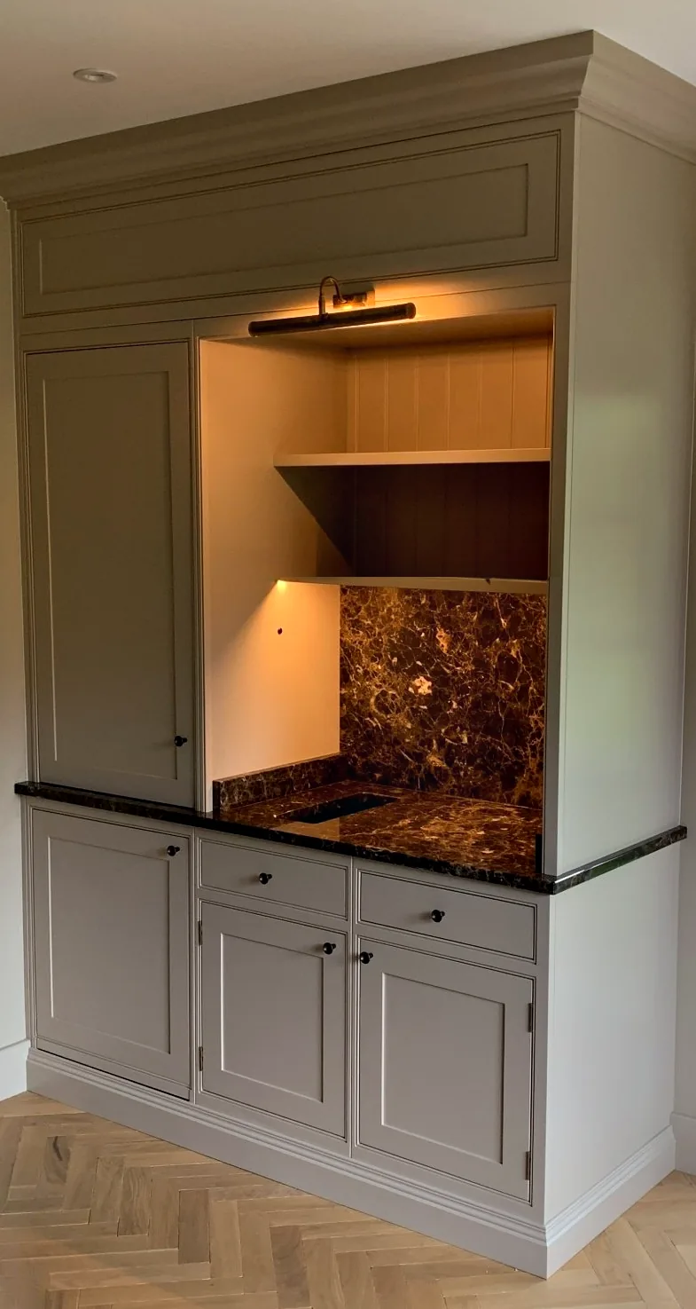 Painted drinks cabinet at Roughwoods with a dark marble worktop and splashback, open shelves and a brass picture light