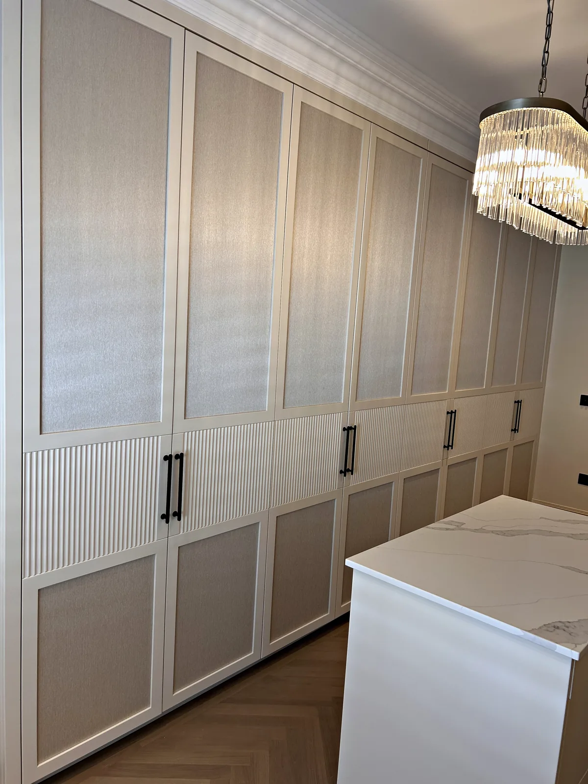 Full height cream wardrobes with textured upper panels, reeded lower panels and black bar handles