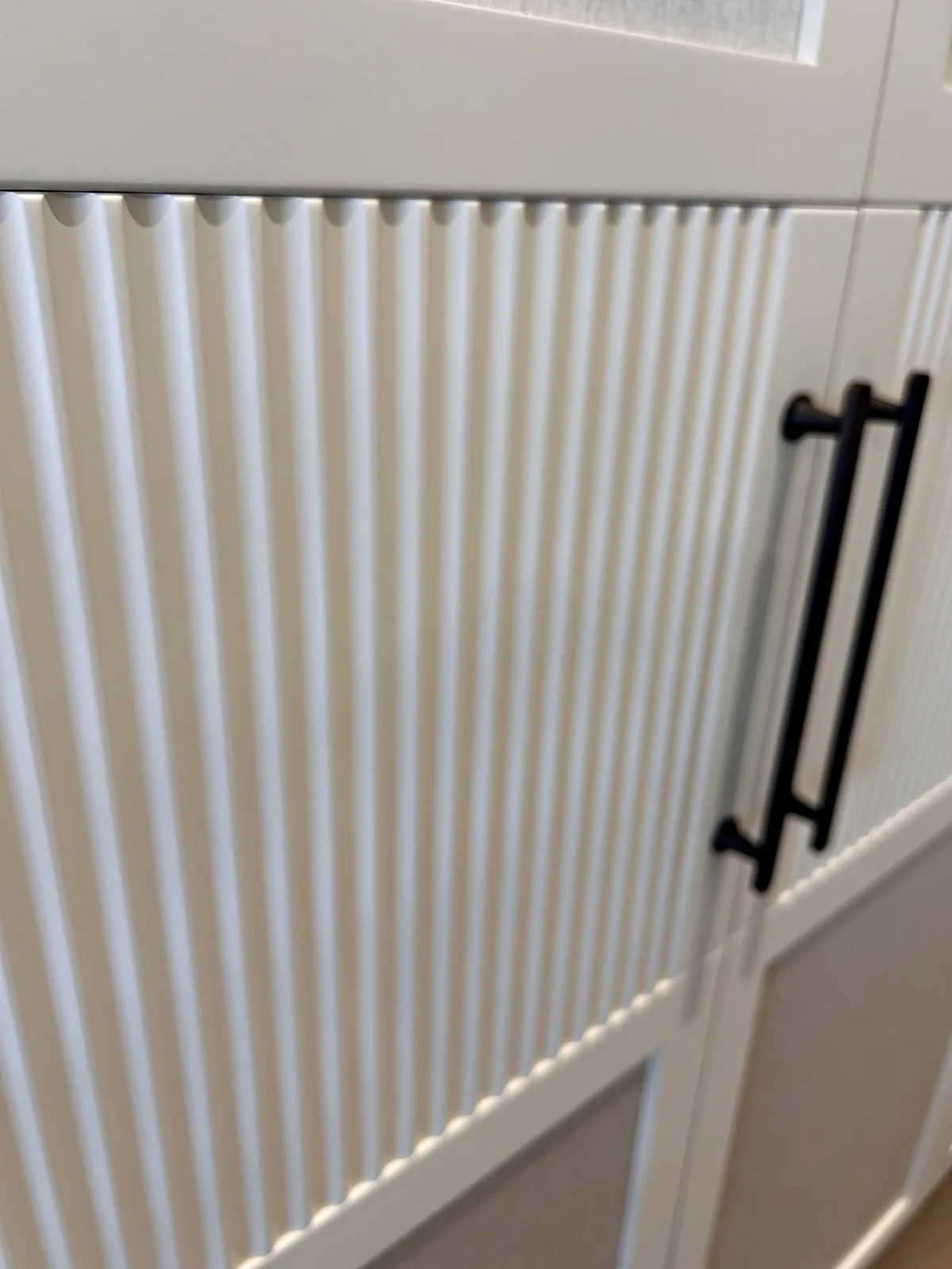 Close view of a cream wardrobe door with a reeded lower panel and a black bar handle