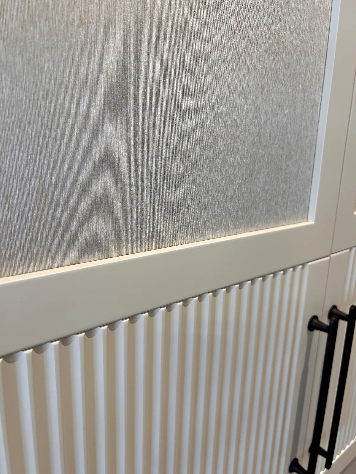 Cream wardrobe door with a textured upper panel, a reeded lower panel and a black bar handle