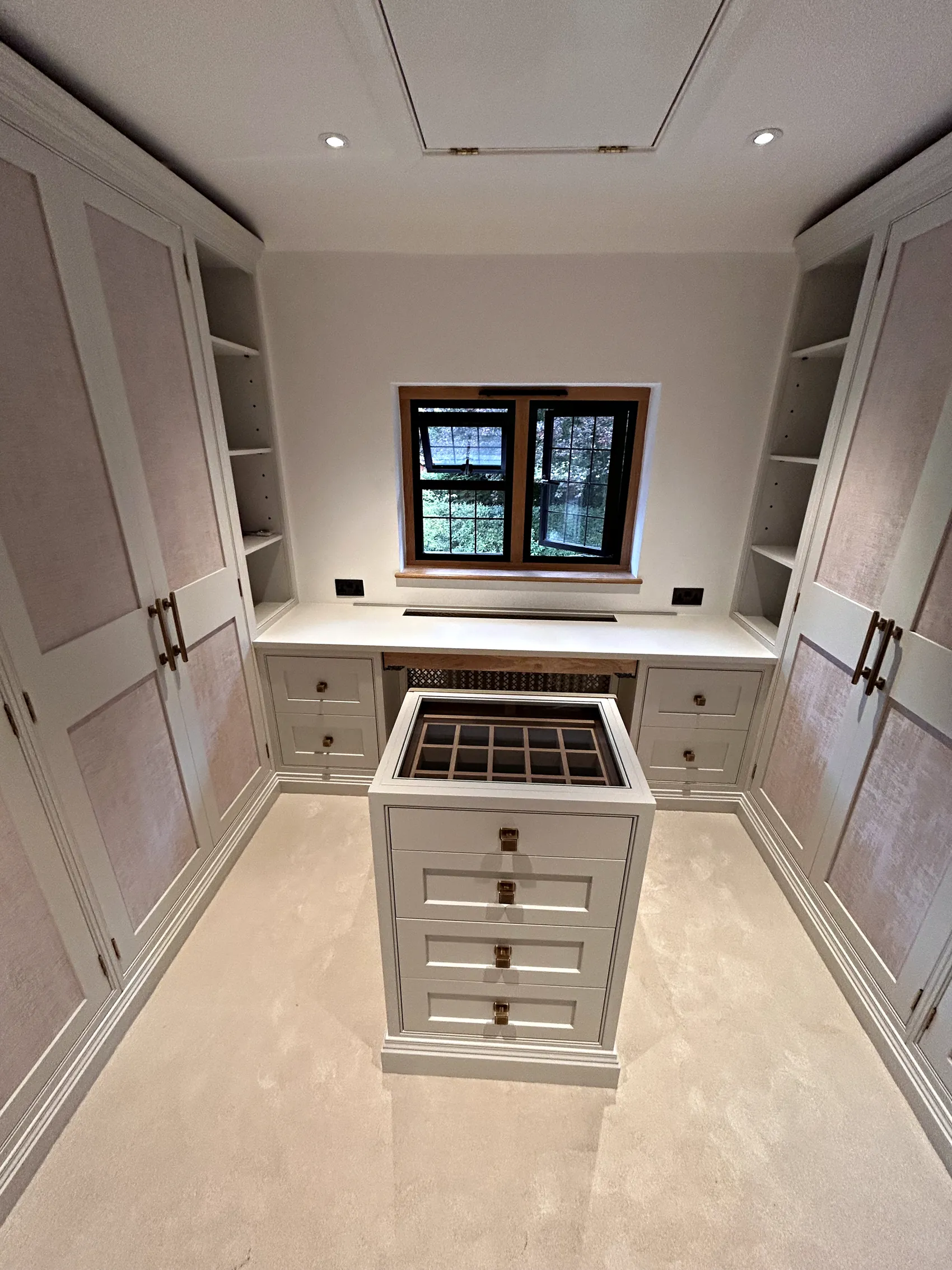 Symmetrical dressing room with wardrobes on both sides, a dressing table under the window and a central drawer island