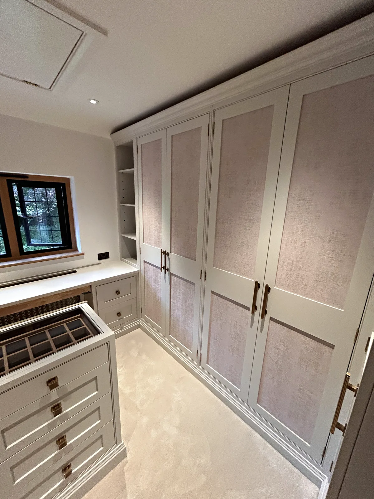 Floor to ceiling wardrobes with blush fabric panels and bronze bar handles in a dressing room