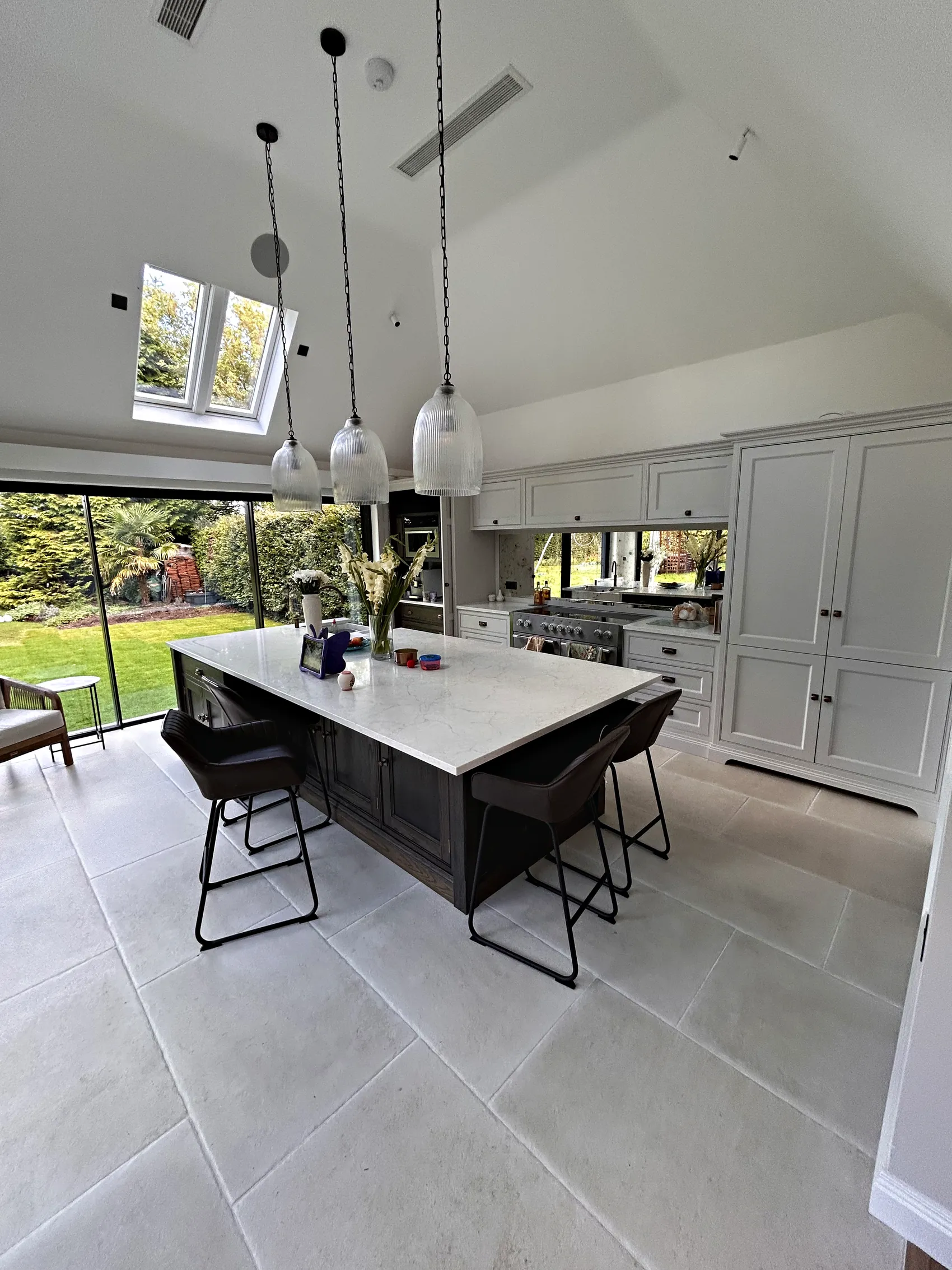 Vaulted kitchen with a dark island and black stools under glass pendants beside the garden doors