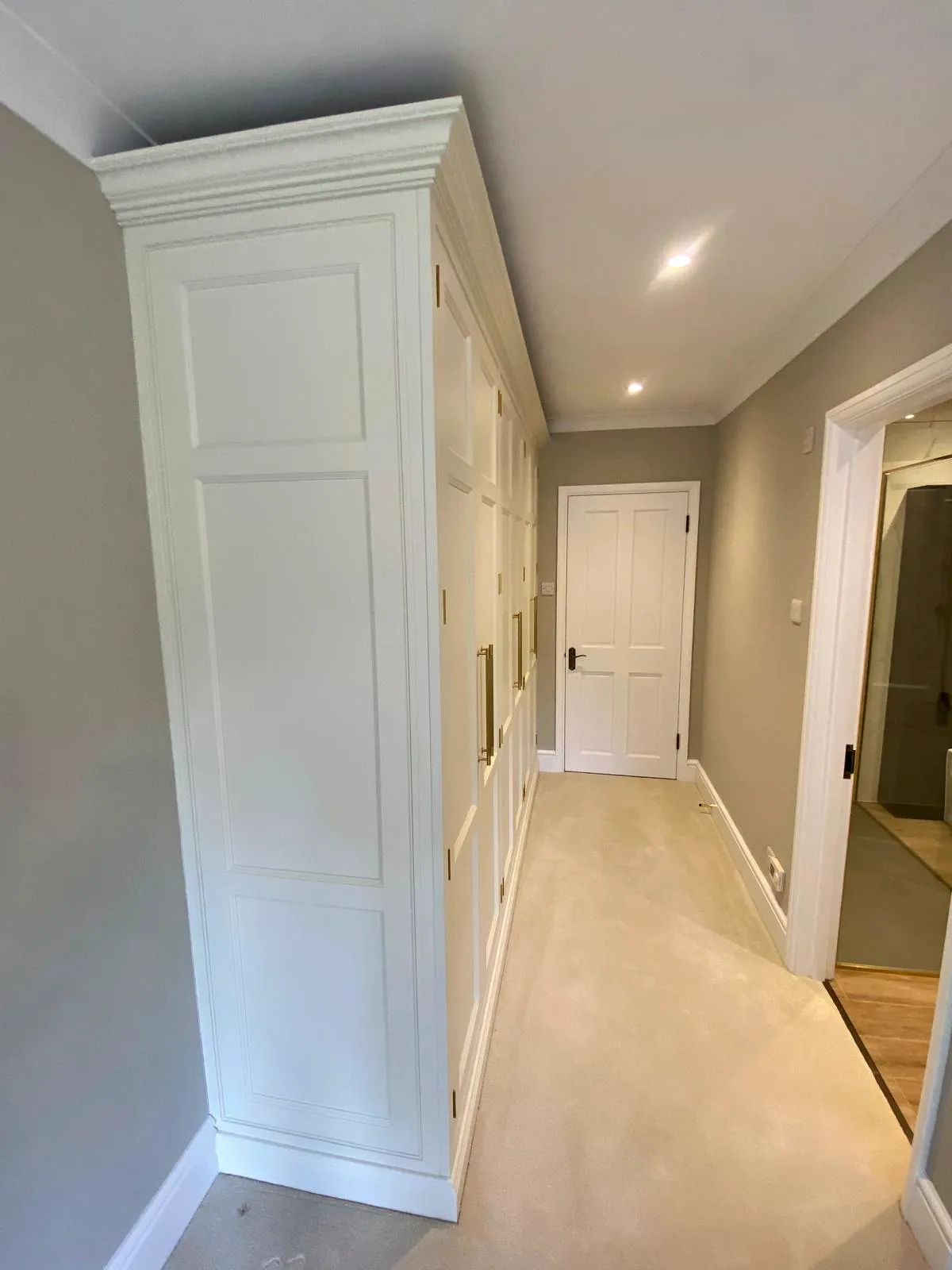 Tall pale grey panelled cupboards with long brass handles running the length of a hallway