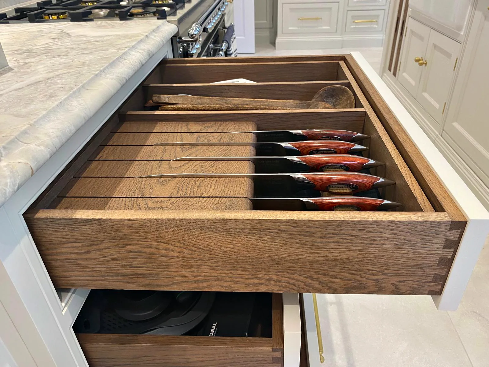 Dark oak dovetailed drawer box pulled open with a knife insert beneath a veined stone worktop