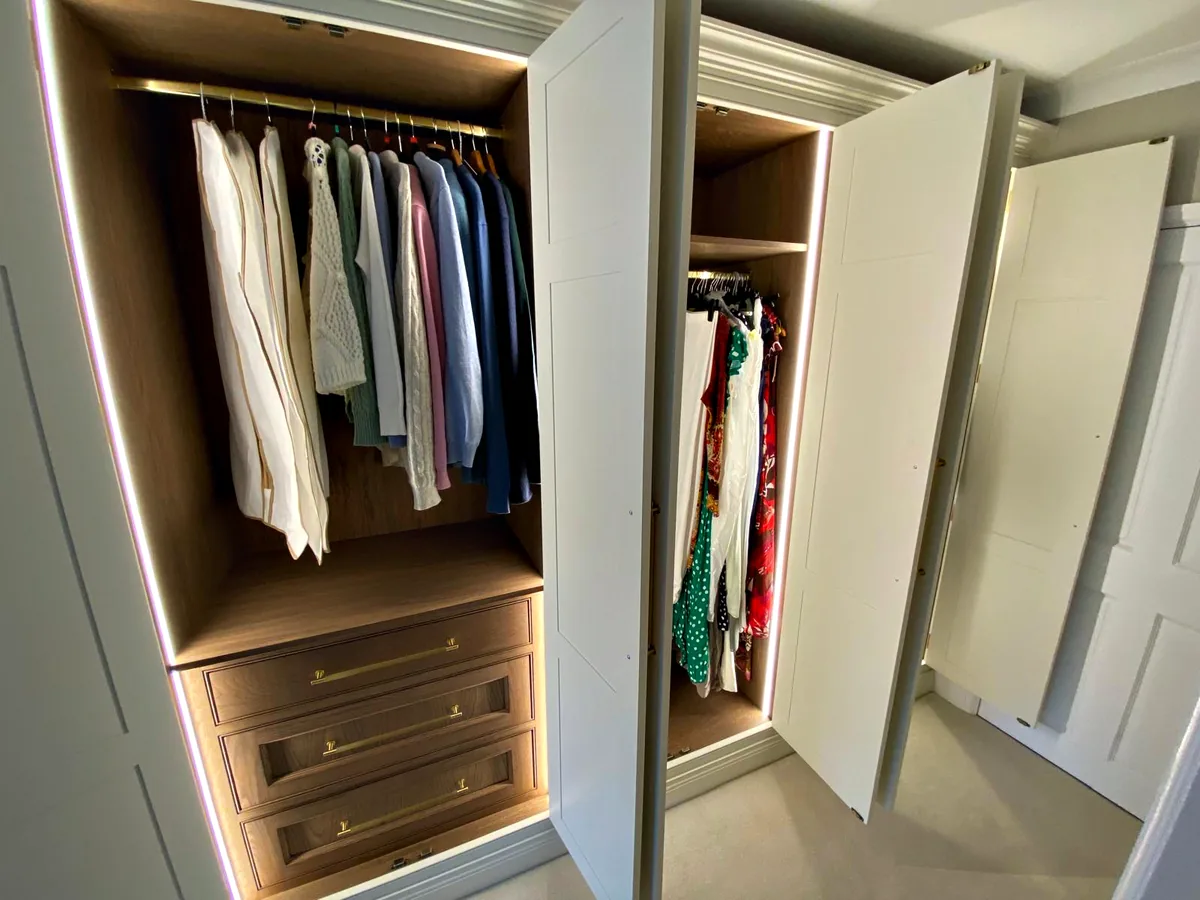 Painted wardrobe doors open on a lit interior with a hanging rail above dark wood drawers