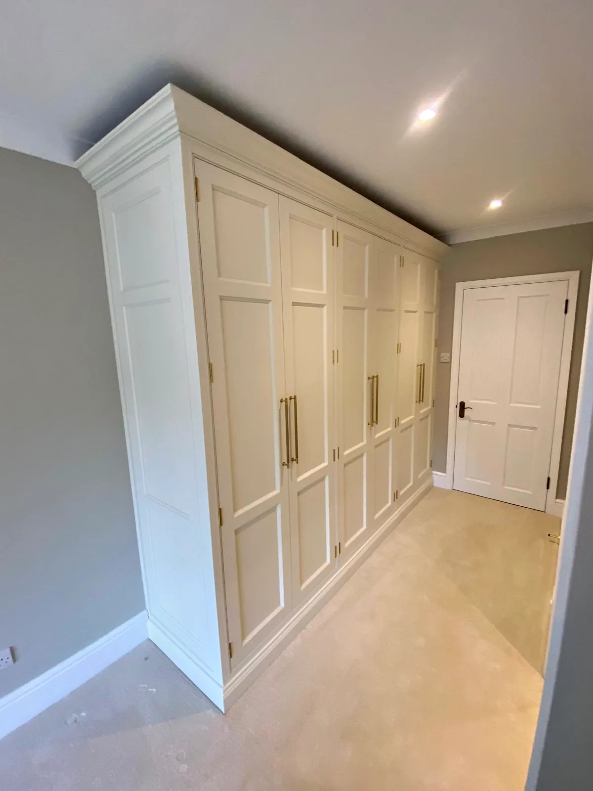 Run of tall pale panelled cupboards with long brass handles beside a doorway