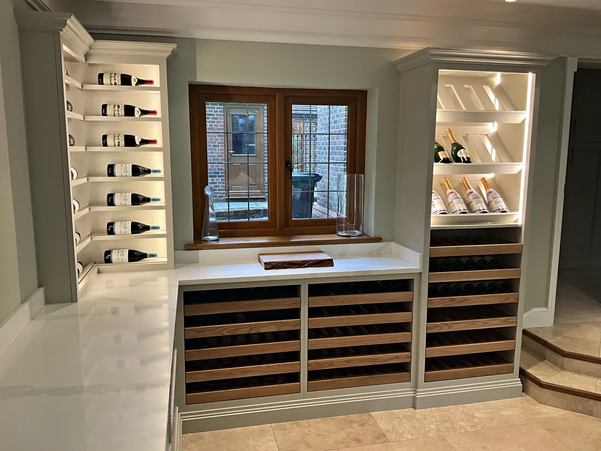 Dining room wine wall with lit display towers of bottles either side of a window and oak pull out wine trays