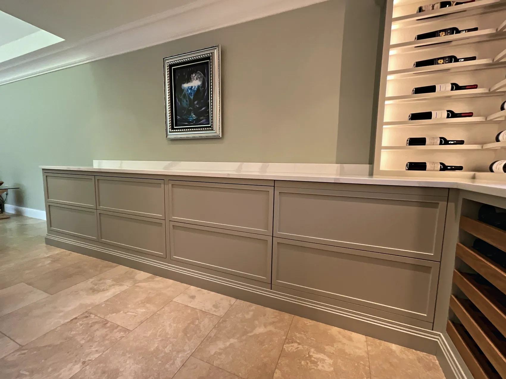 Long run of panelled sage grey sideboard cupboards meeting a lit wine tower
